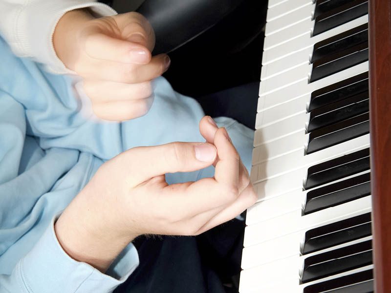 Hände spielen Klavier, während eine andere Hand eine Geste zeigt.