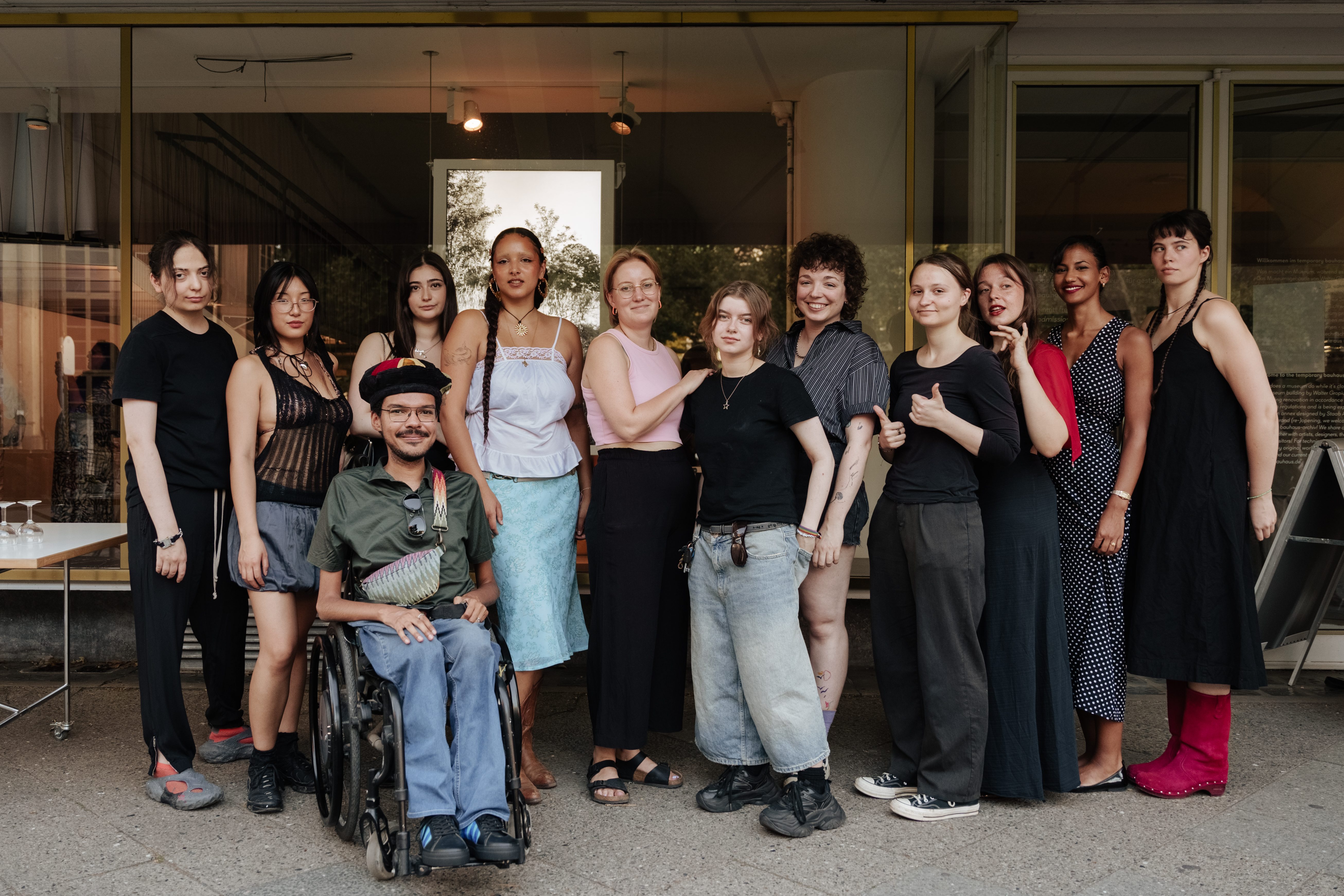 Gruppe von 14 Personen, darunter Frauen und eine Person im Rollstuhl, posiert freundlich vor einem Gebäude.