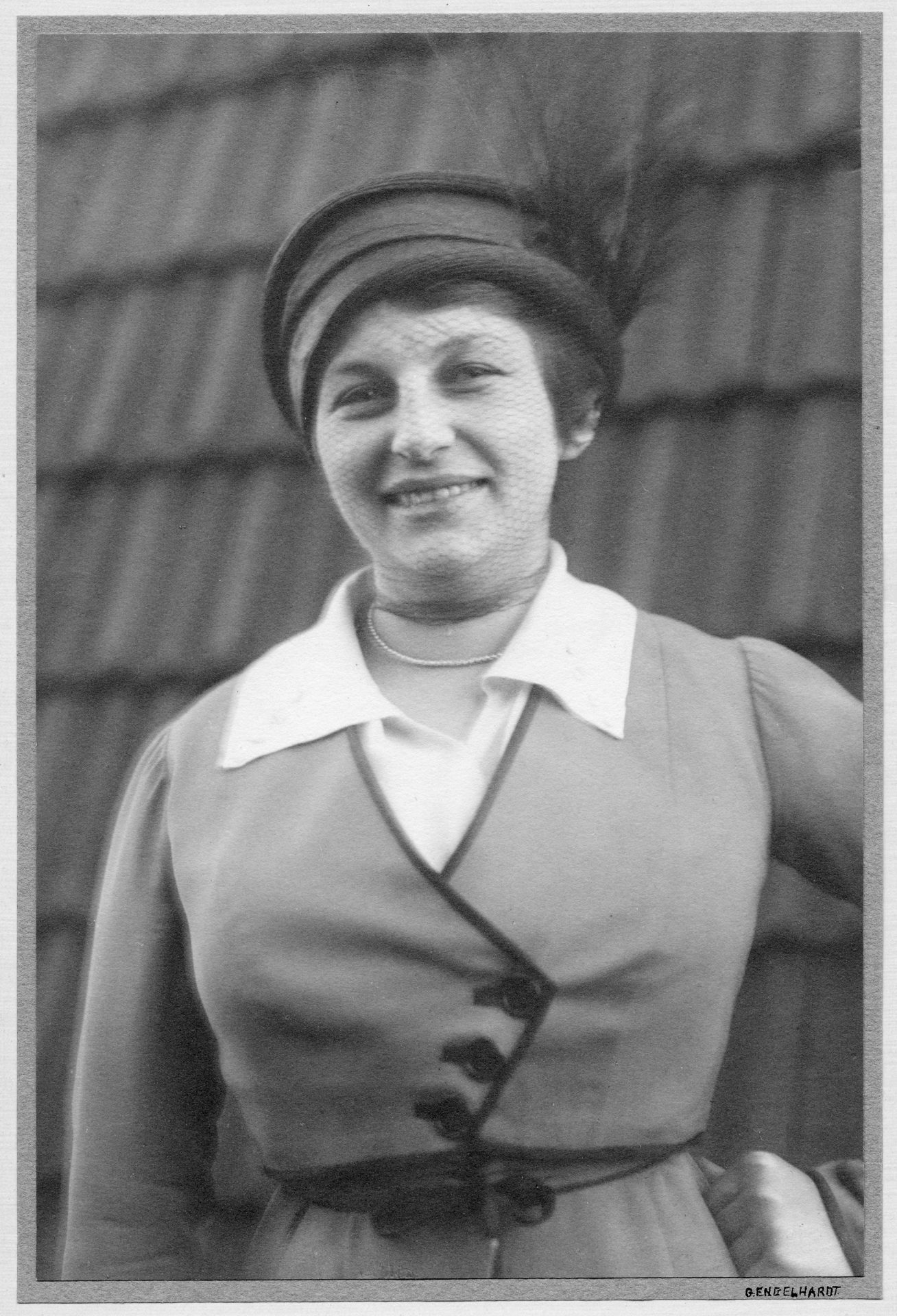 Frauenporträt in Schwarz-Weiß, lächelnd, mit einem Hut und einem eleganten Kleid mit weißen Kragen.