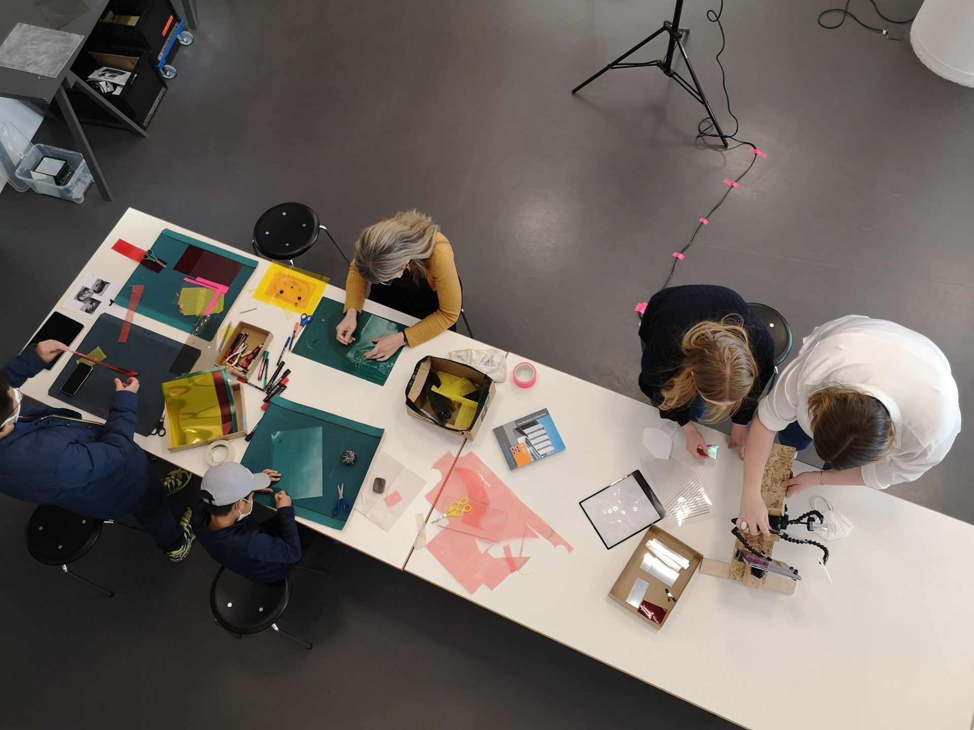 Personen sind kreativ am Tisch mit buntem Material, Scheren und Bastelutensilien beschäftigt.