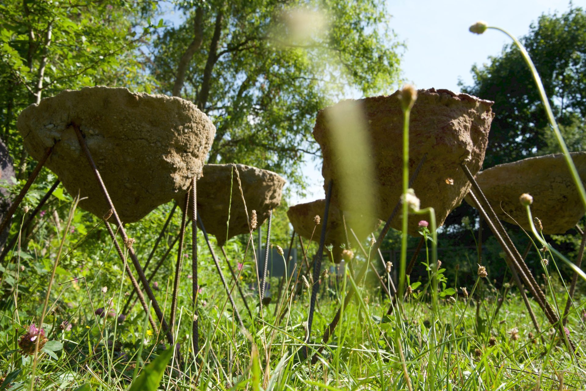 Kunstvolle Gartenmöbel aus Beton mit Metallbeinen, umgeben von grüner Wiese und Pflanzen im Sonnenlicht.