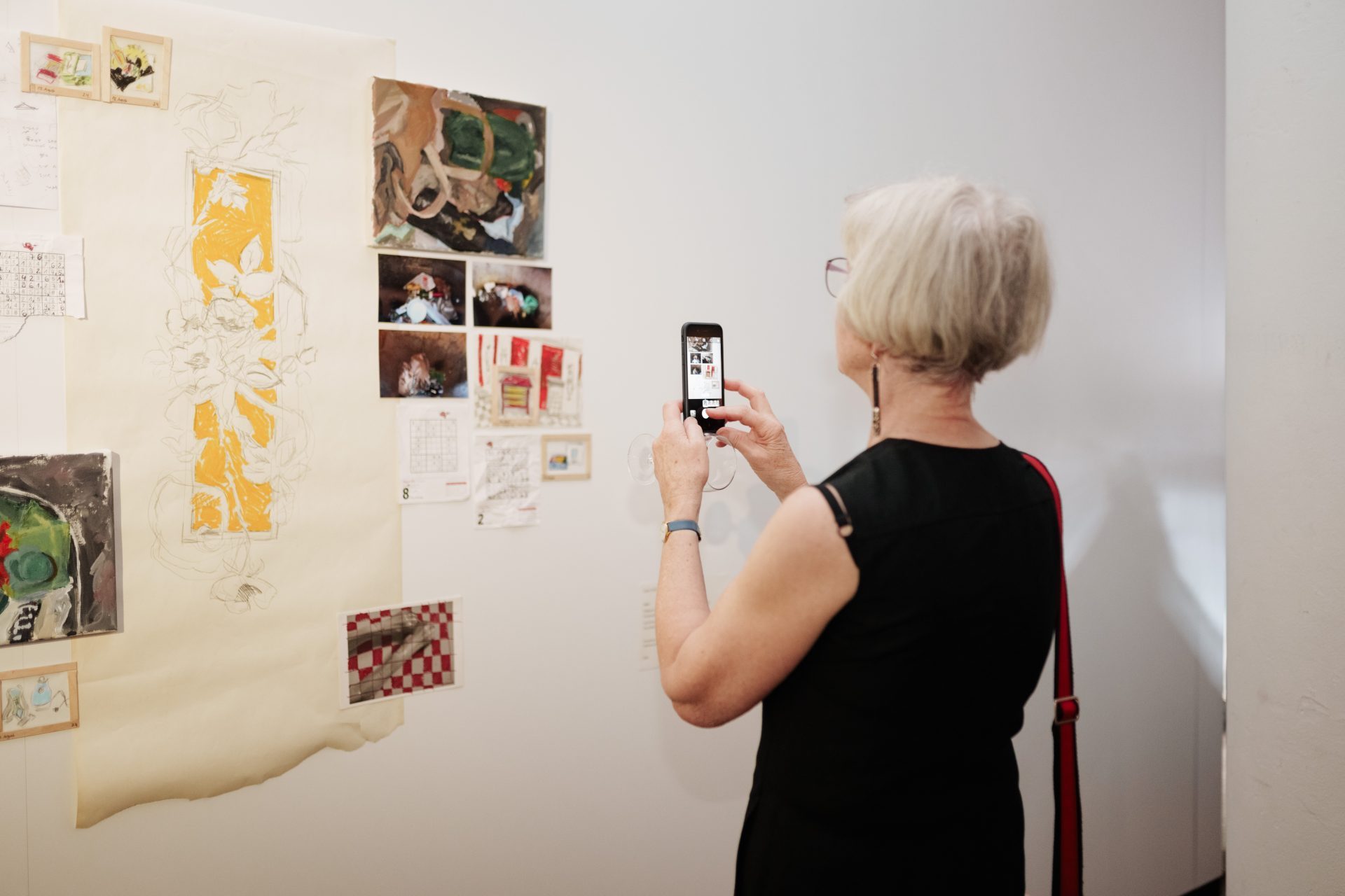 Frau fotografiert eine Galeriewand mit verschiedenen Kunstwerken und Notizen.
