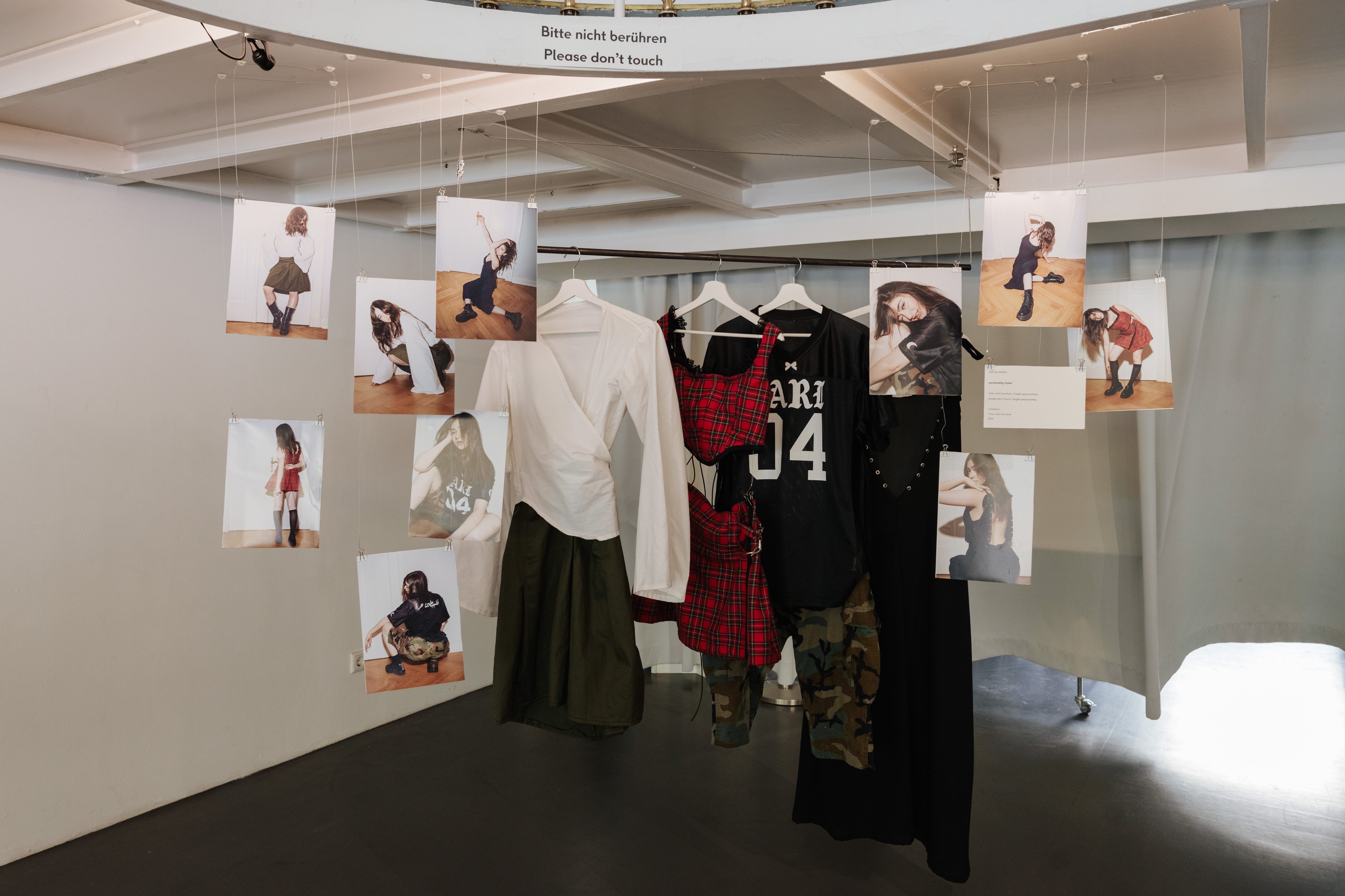 Modeausstellung mit Fotos und Kleidungsstücken an Bügeln, Hinweis: "Bitte nicht berühren".