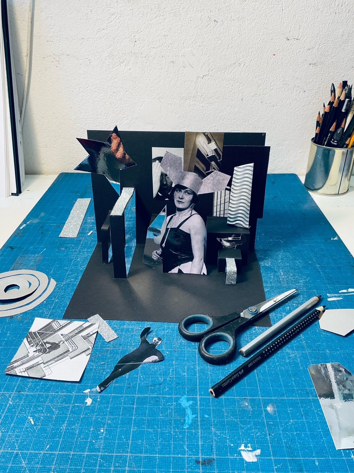 Kreatives Collagenprojekt mit Fotos und geometrischen Formen auf einem Tisch, umgeben von Bastelmaterialien.