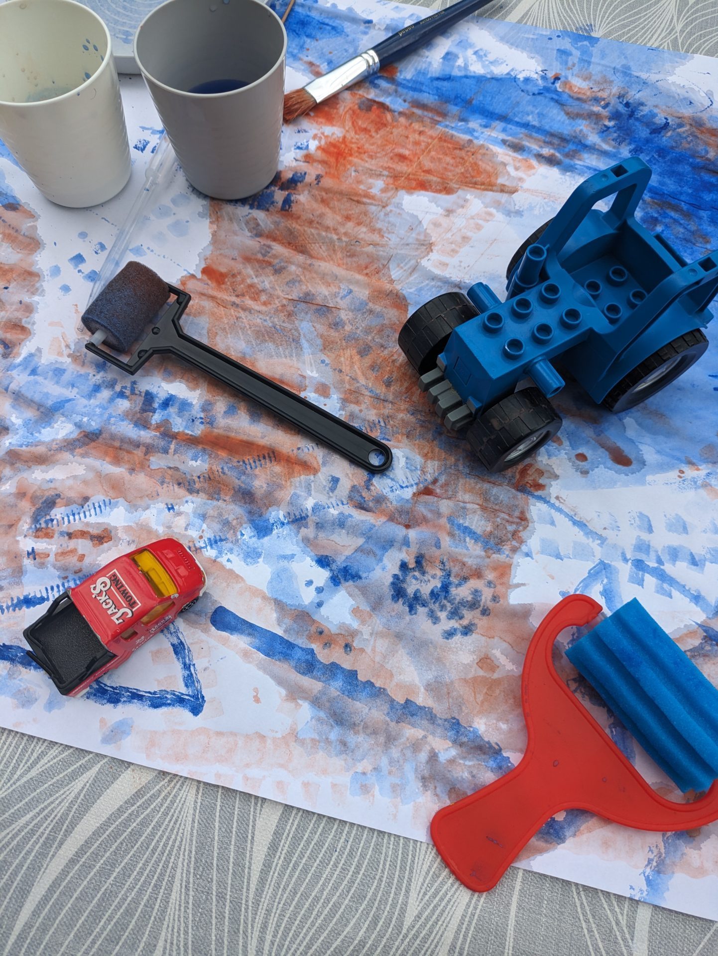 Colorful art supplies, including a blue toy tractor, paint buckets, and painting tools on paper.