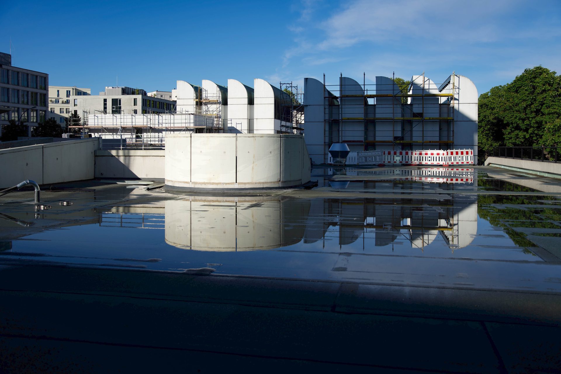 Modernes Baustellengelände mit spiegelnden Flächen und strahlend blauem Himmel im Hintergrund.