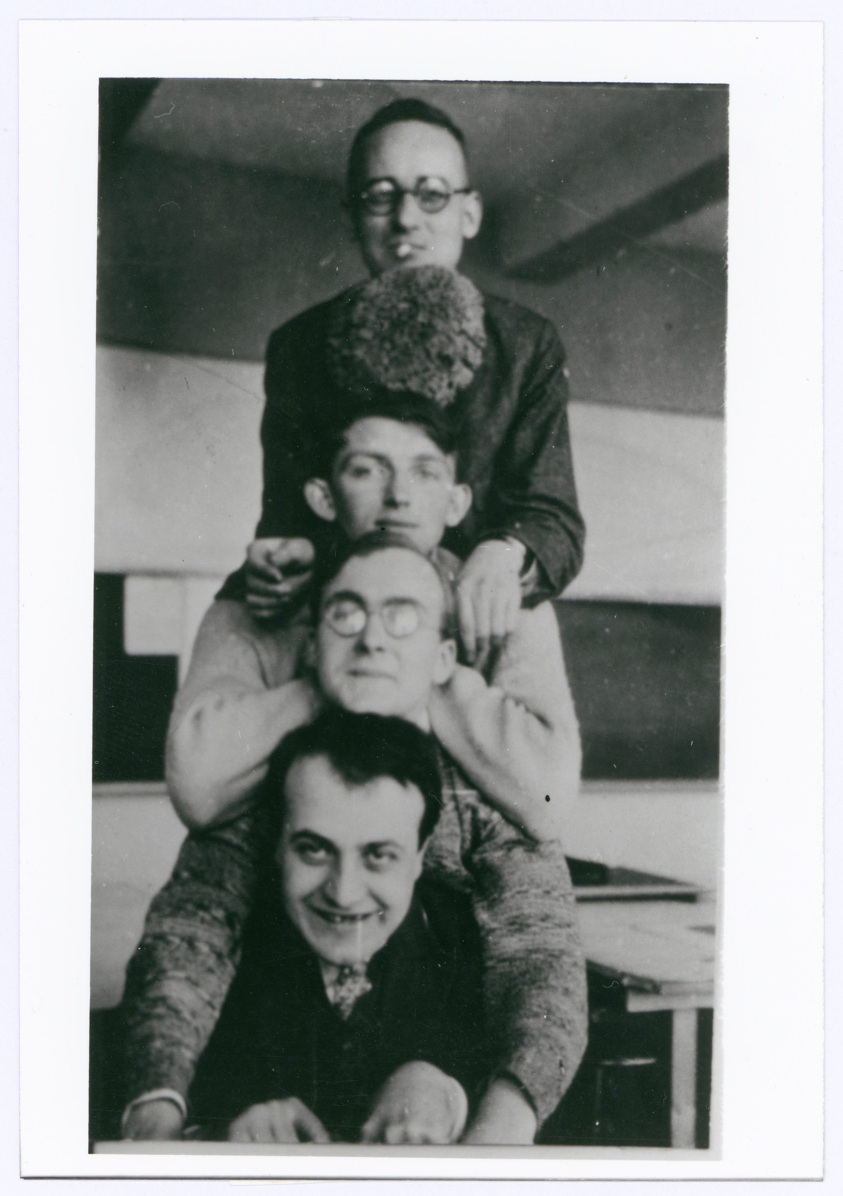Vier Personen stehen übereinander, lachen und posieren in einem Retro-Klassenzimmer.