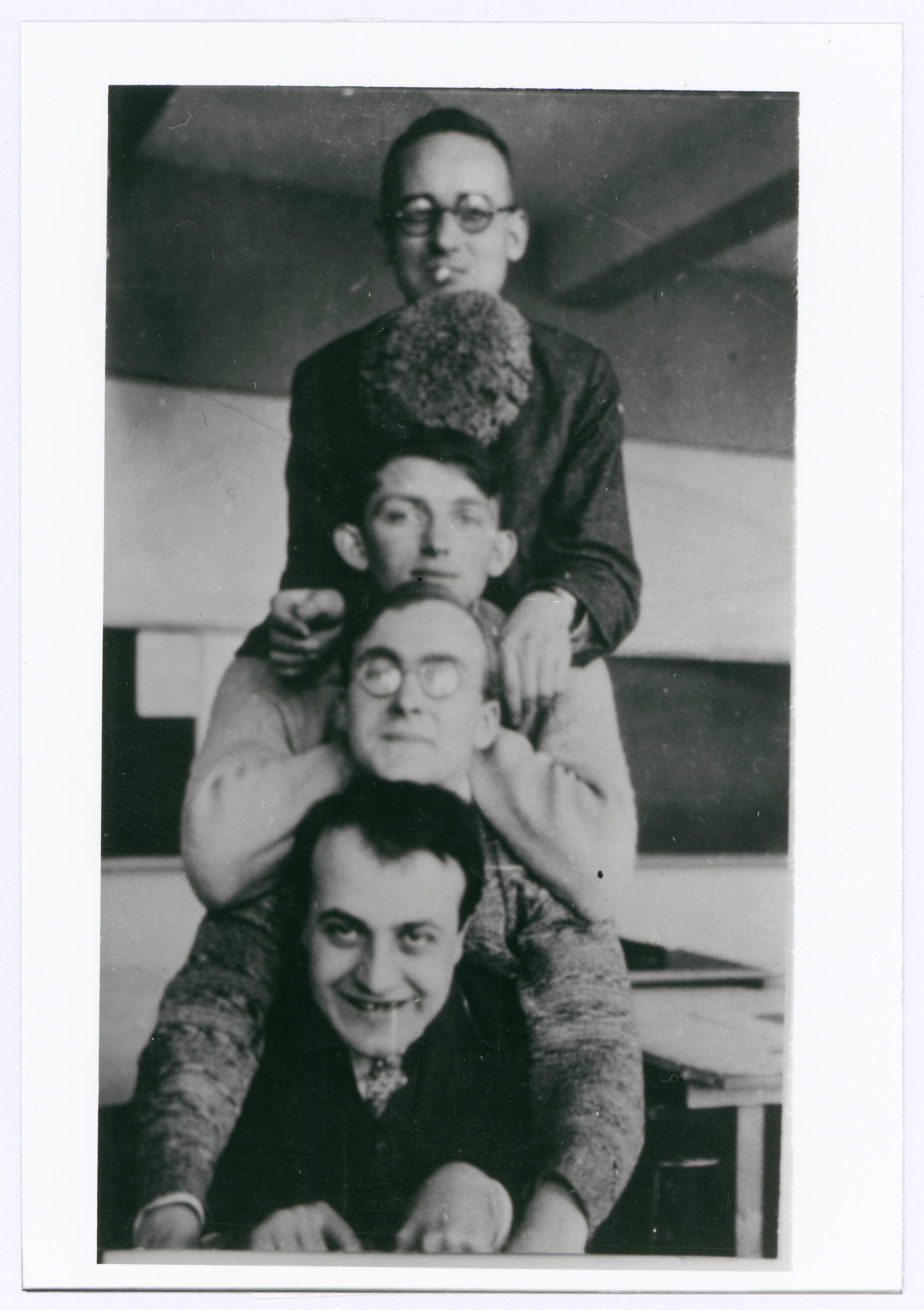 Four people are stacked on top of each other, laughing and posing in a retro-style classroom.