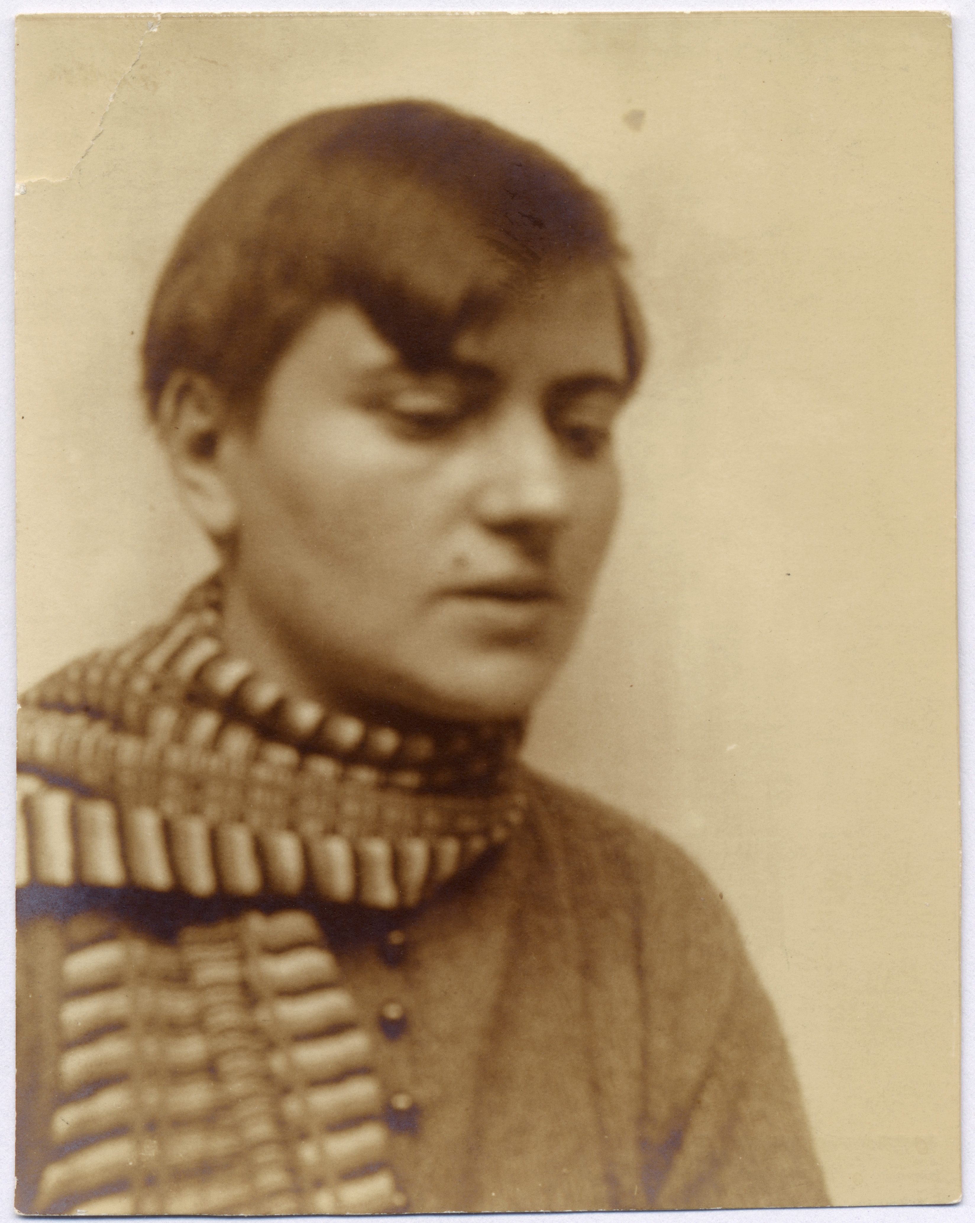 Portrait of a person with short hair wearing a scarf against a sepia background.