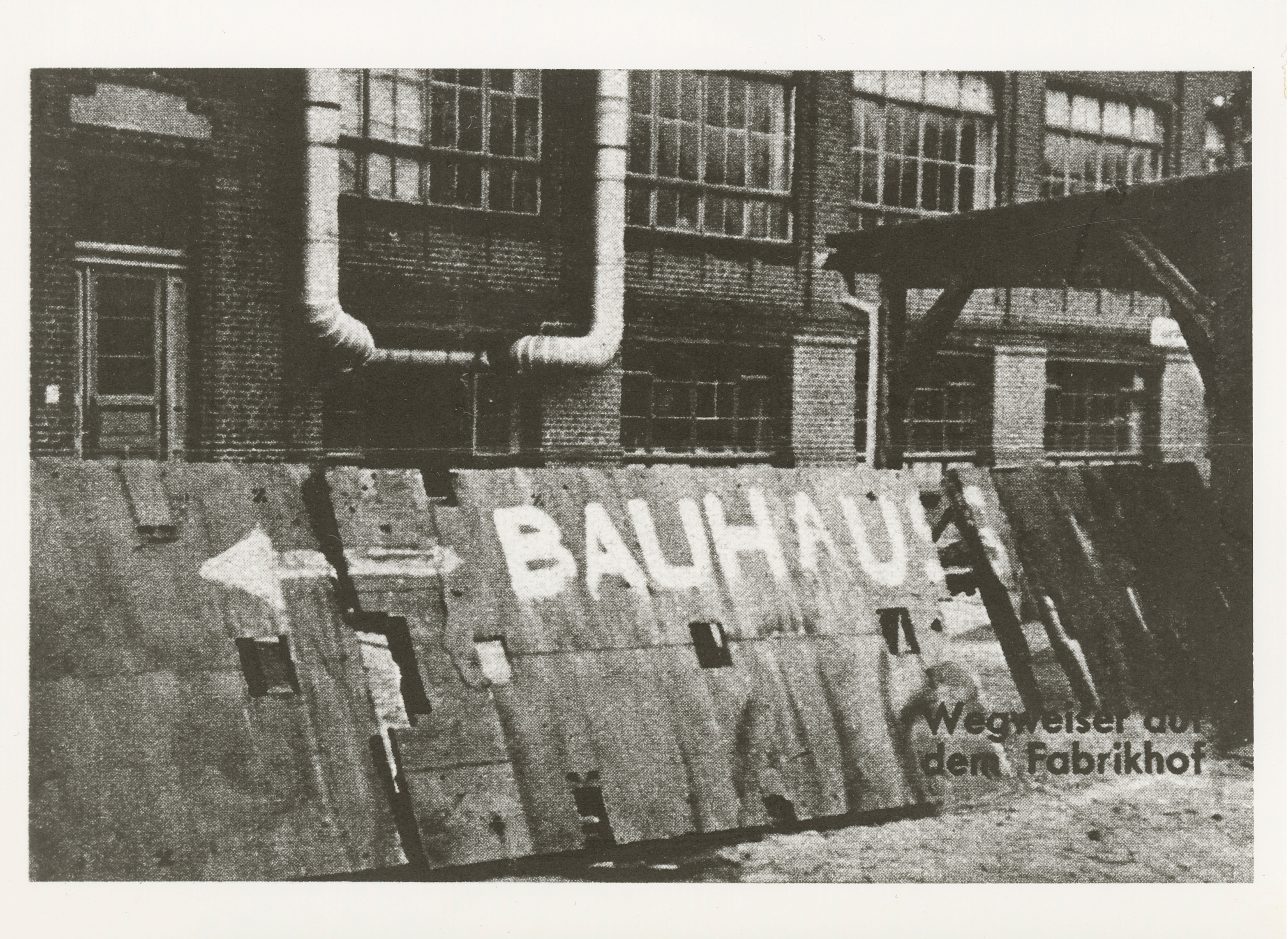 Historisches Schwarz-Weiß-Bild einer Wand mit dem Wort "BAUHAUS" und einem Pfeil zum Fabrikhof.