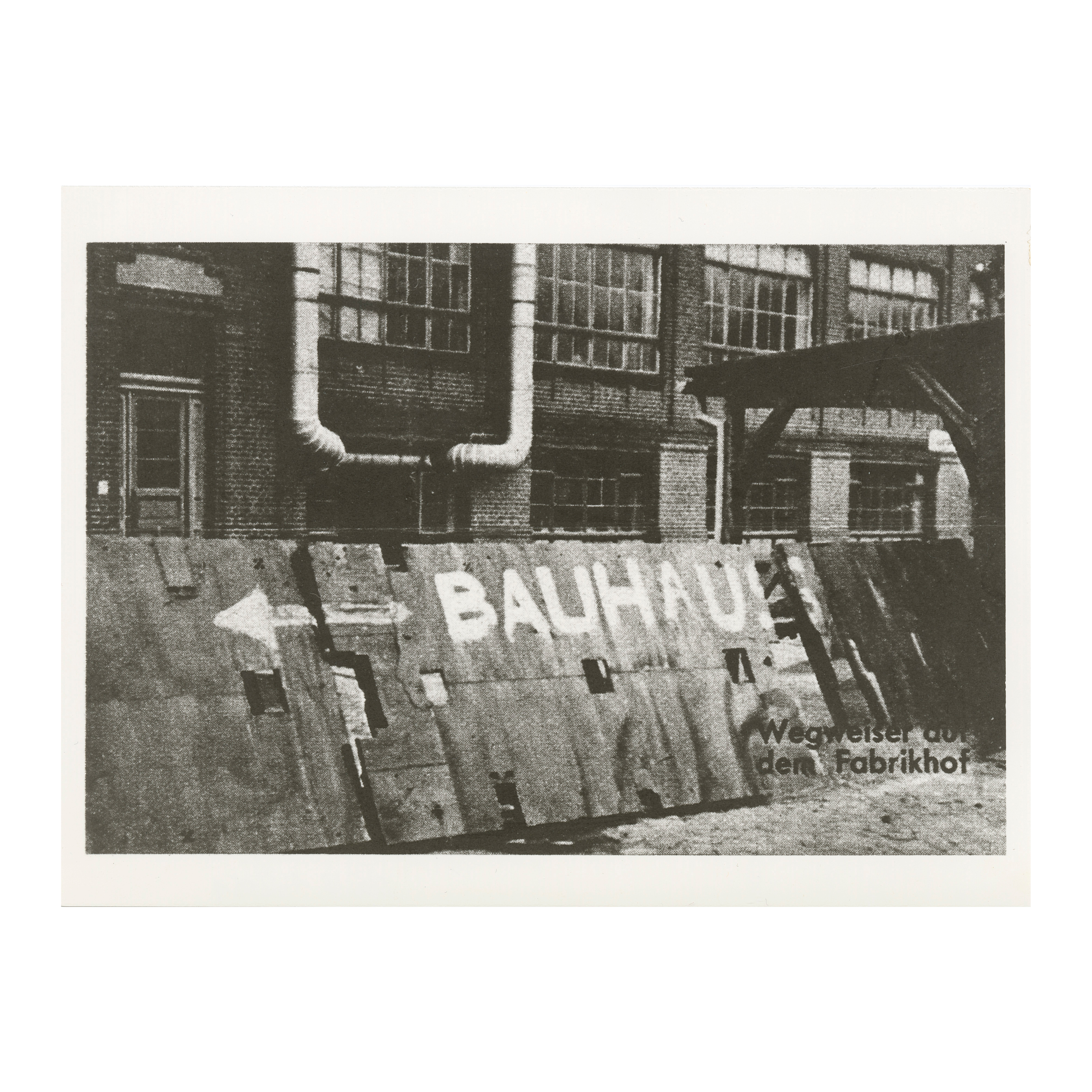 Historical black-and-white image of a wall with the inscription "BAUHAUS" and an arrow pointing to the factory yard.