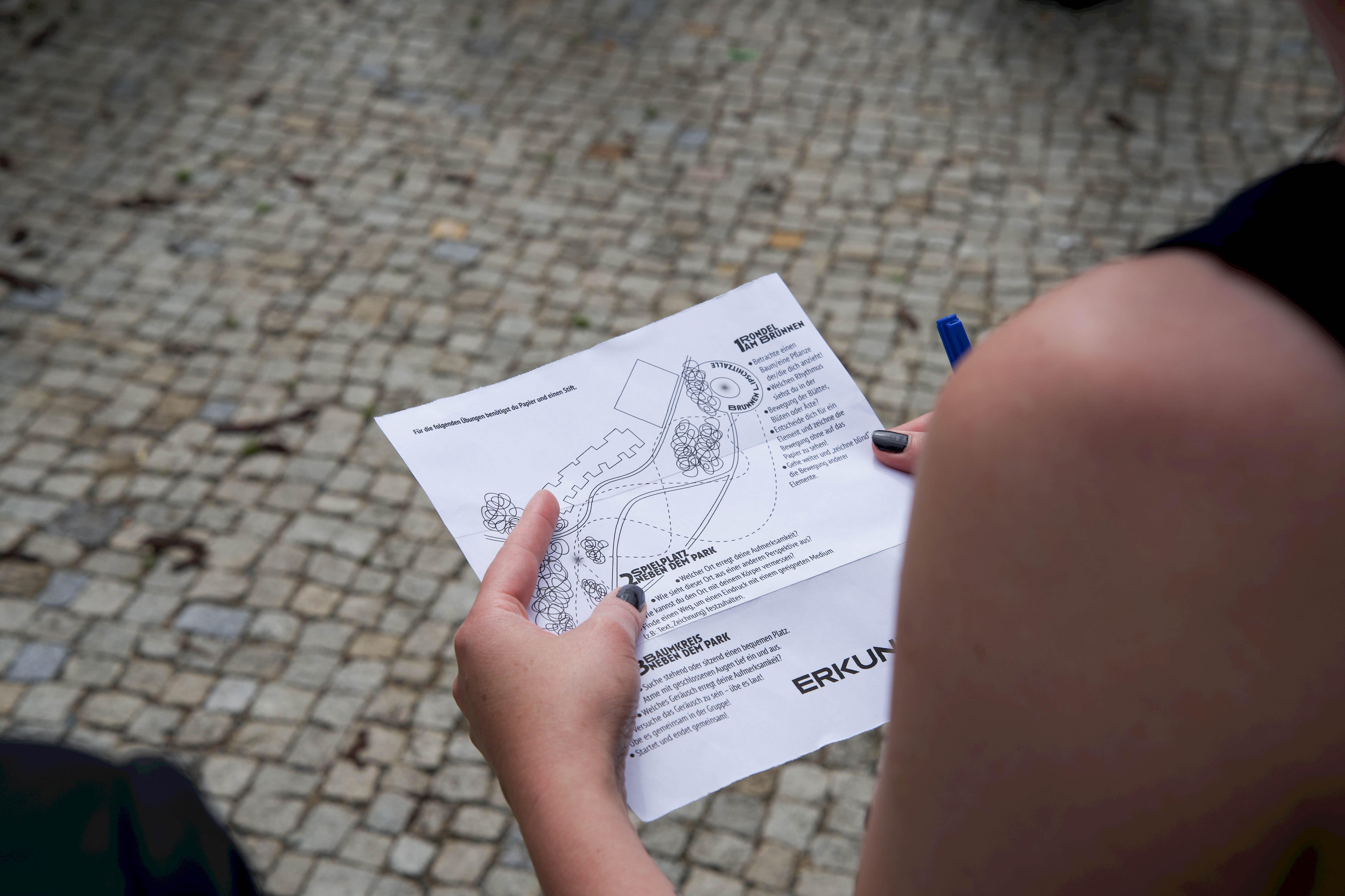 Eine Person hält einen Stadtplan mit Informationen und Markierungen auf einem gepflasterten Boden.
