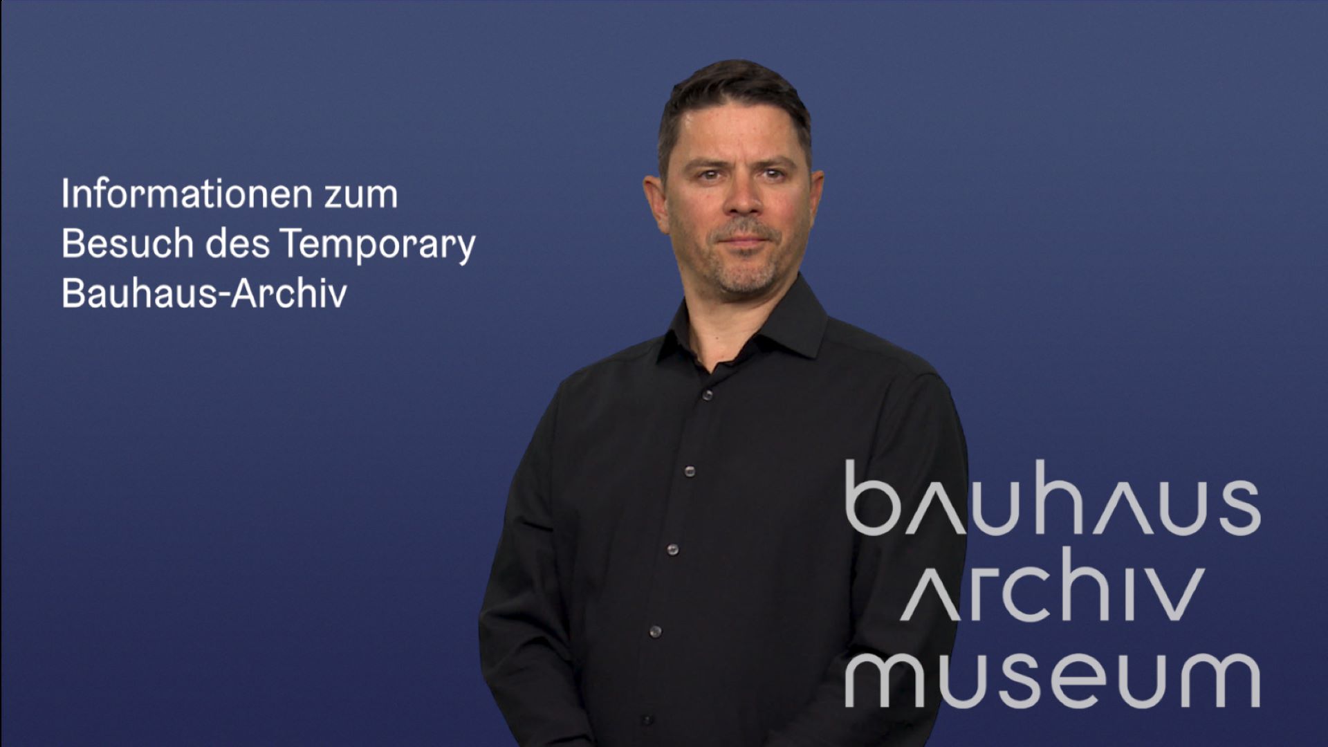 Mann in schwarzem Hemd präsentiert Informationen zum Besuch des Temporary Bauhaus-Archivs vor blauem Hintergrund.