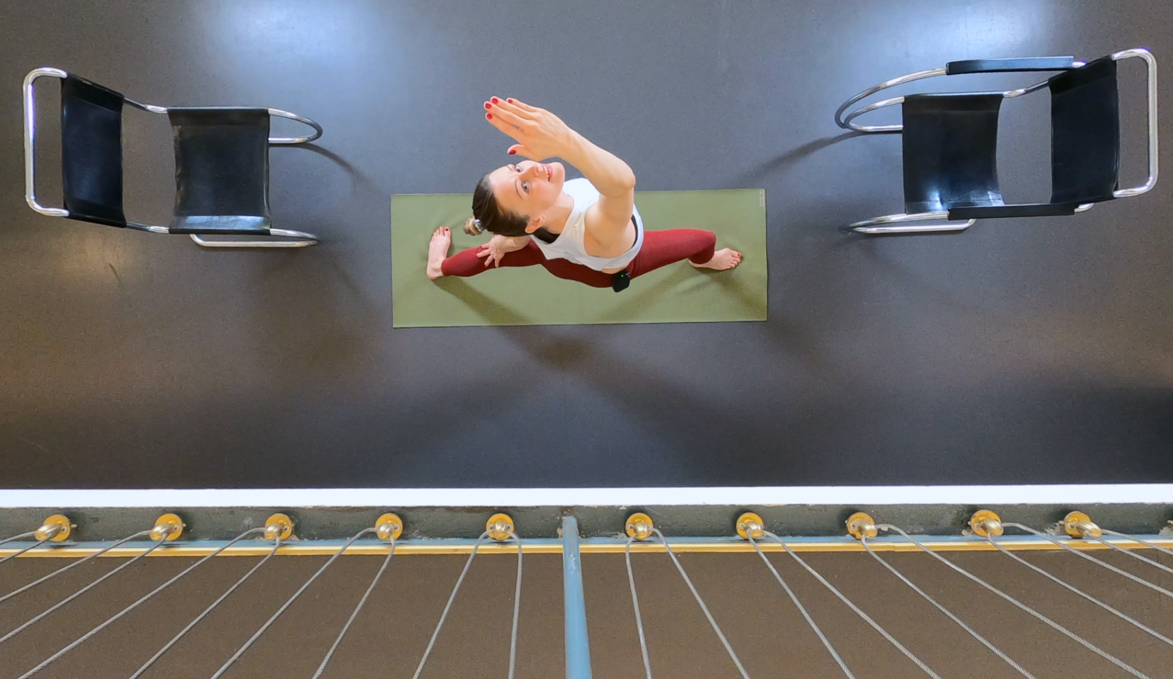 Frau in Yogapose auf einer Matte, umgeben von zwei Stühlen, aus der Vogelperspektive aufgenommen.
