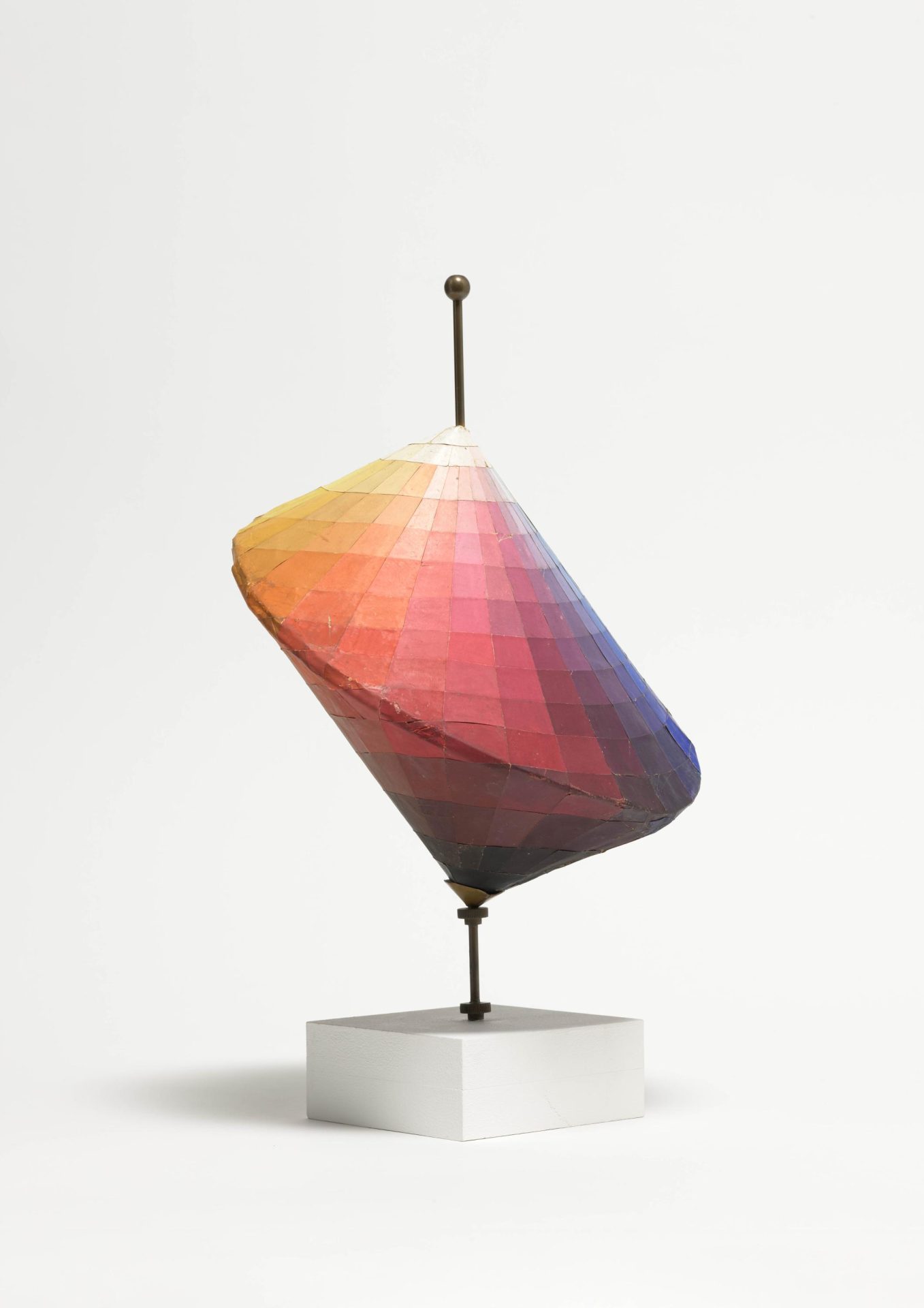Abstrakte Skulptur in Kegelform mit bunten, geometrischen Flächen auf einer weißen Basis.