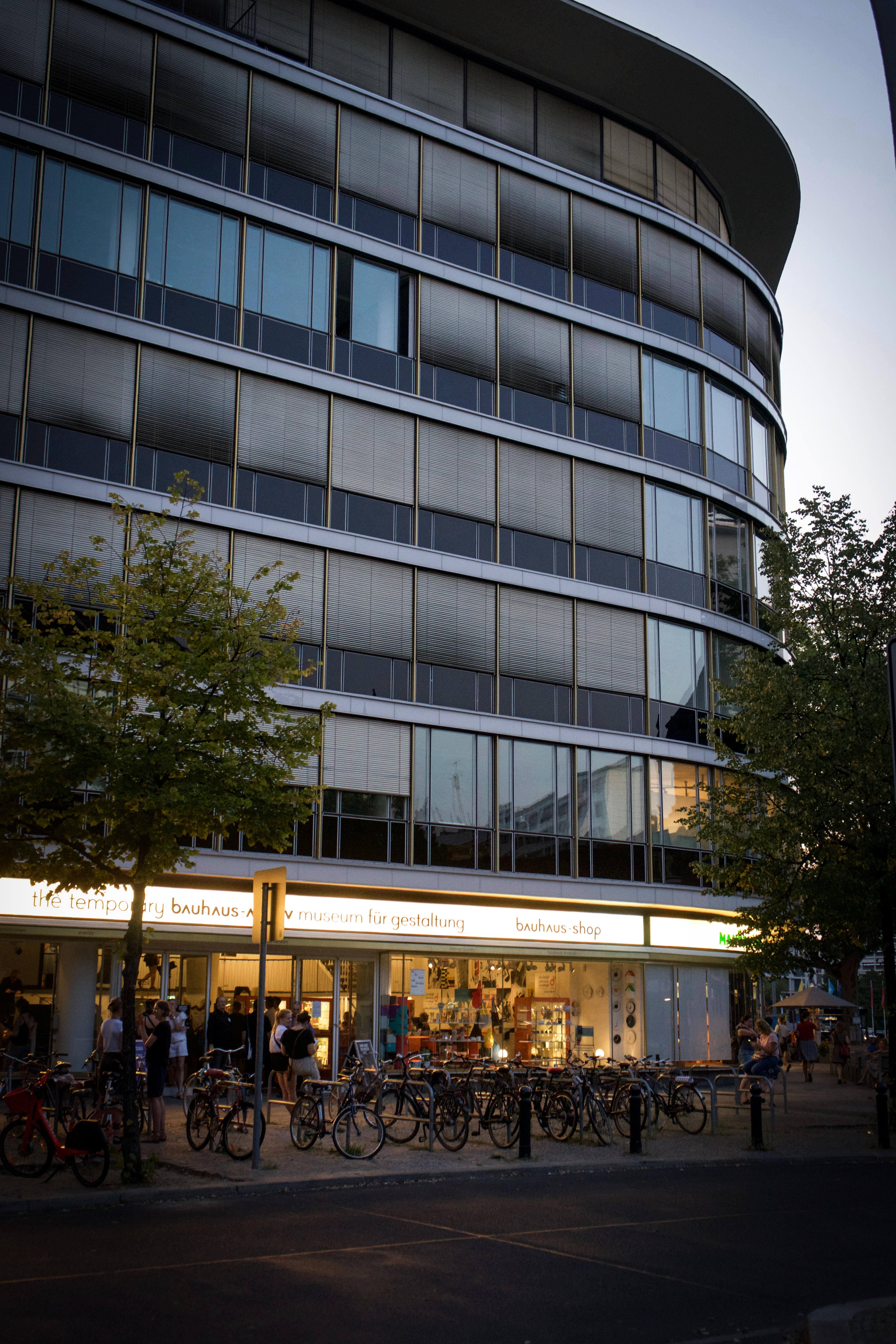 Moderne Geschäftsgebäude mit großen Fenstern, beleuchtetem Eingangsbereich und Fahrrädern davor, bei Dämmerung fotografiert.