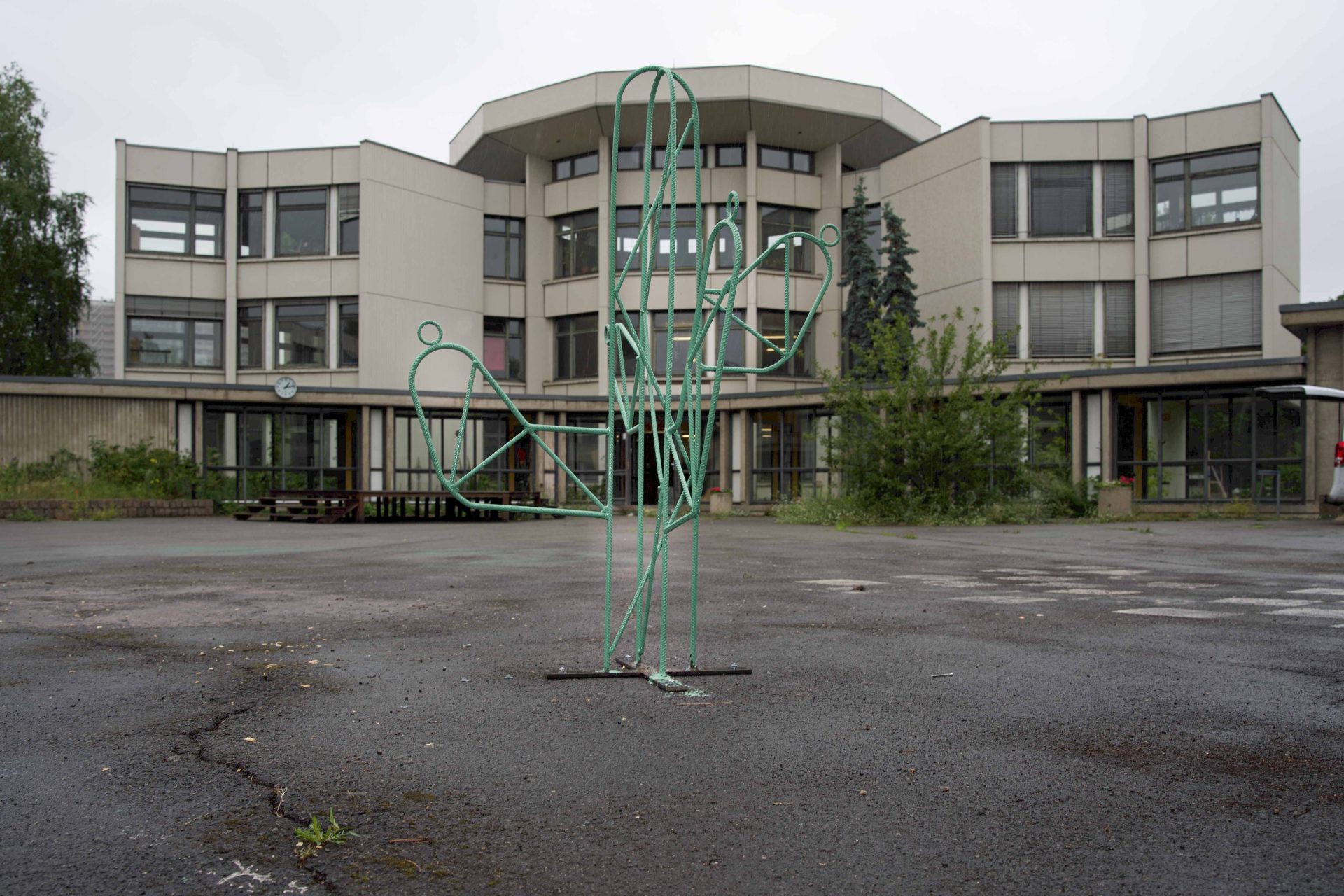 Kunstinstallation eines grünen Cactus vor einem modernen Gebäude, bei bewölkten Wetterbedingungen.