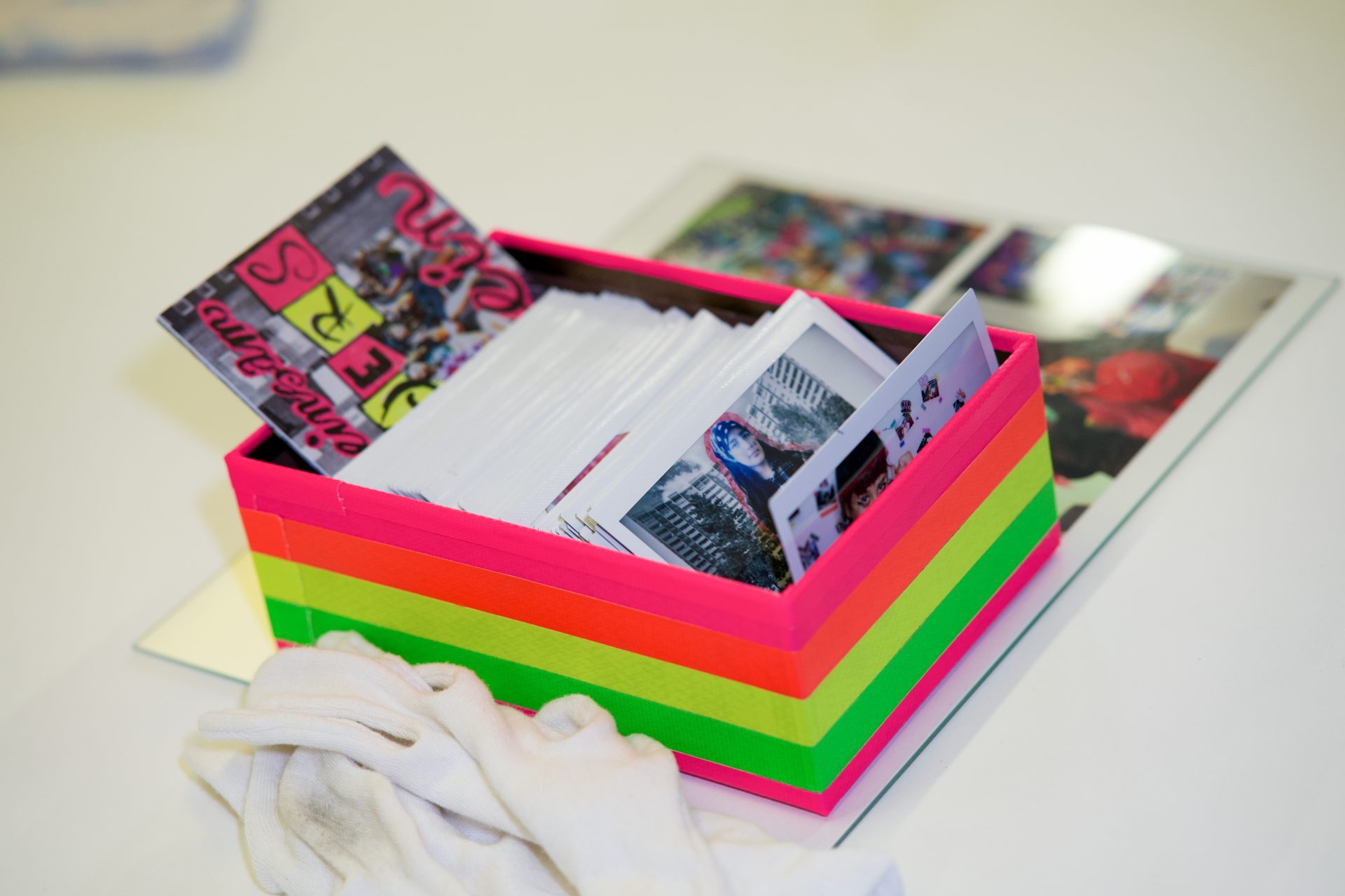 Bunte Kiste mit Fotos und Zeitschriften, neben einem weißen Tuch und weiteren Bildern auf dem Tisch.