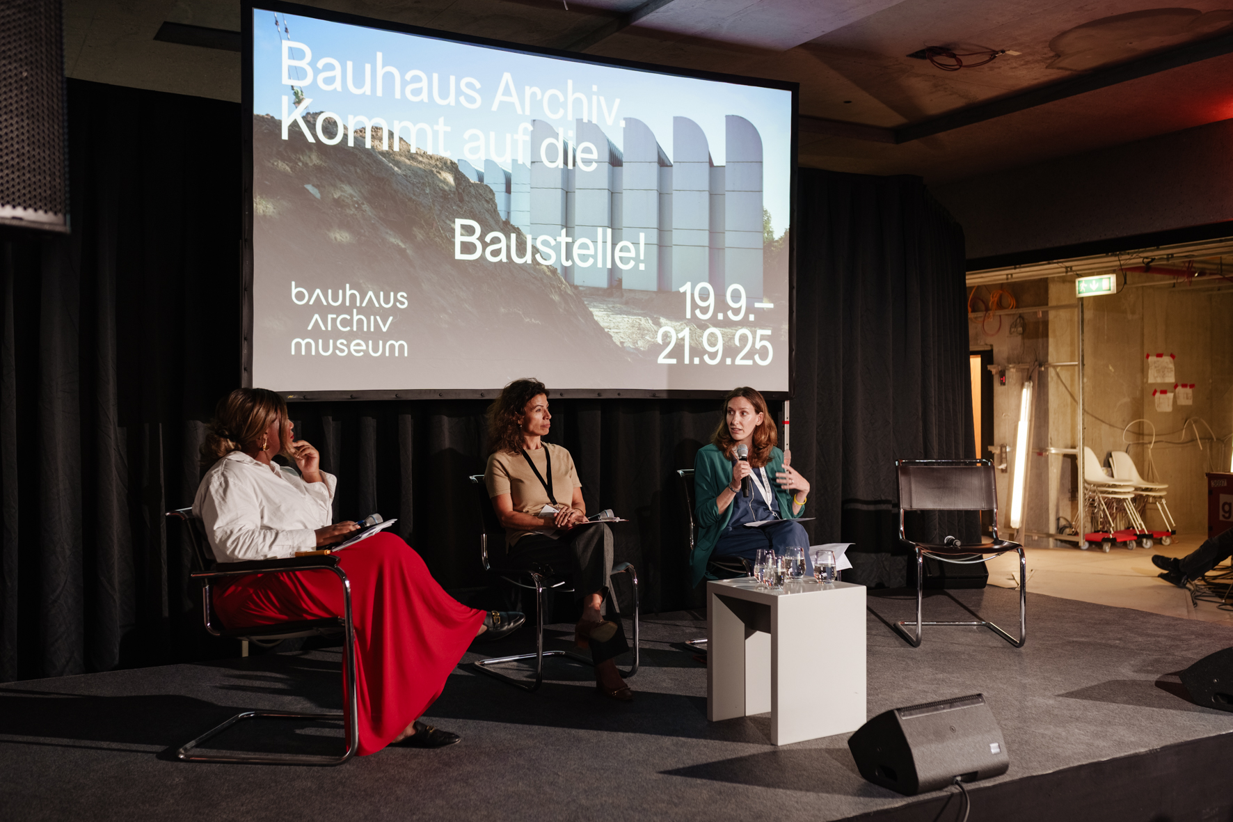 Paneldiskussion im Bauhaus-Archiv mit drei Rednerinnen, im Hintergrund ein Bildschirm mit Hinweisen zur Veranstaltung.