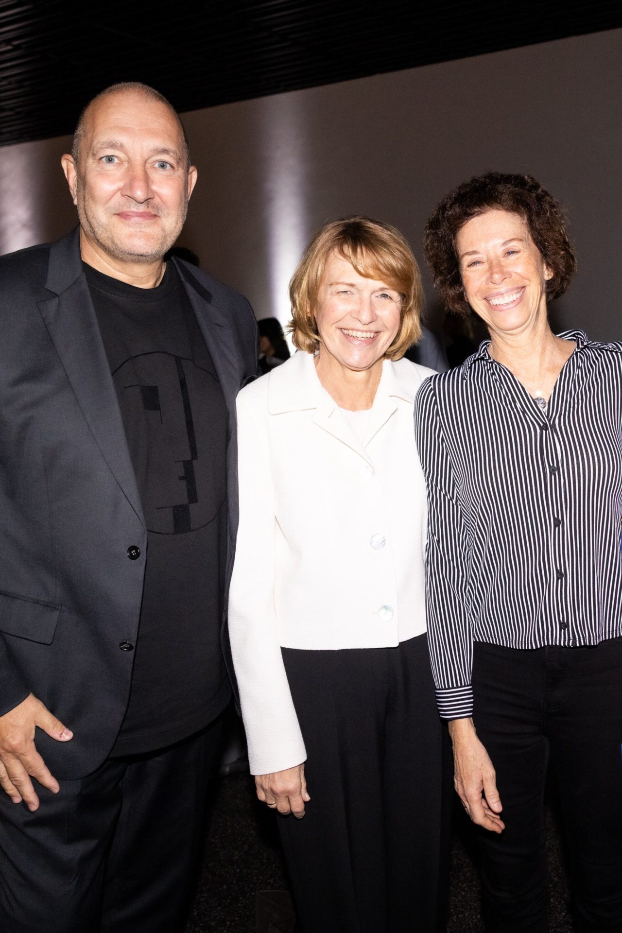 Three smiling individuals pose together in a modern venue with dim lighting.