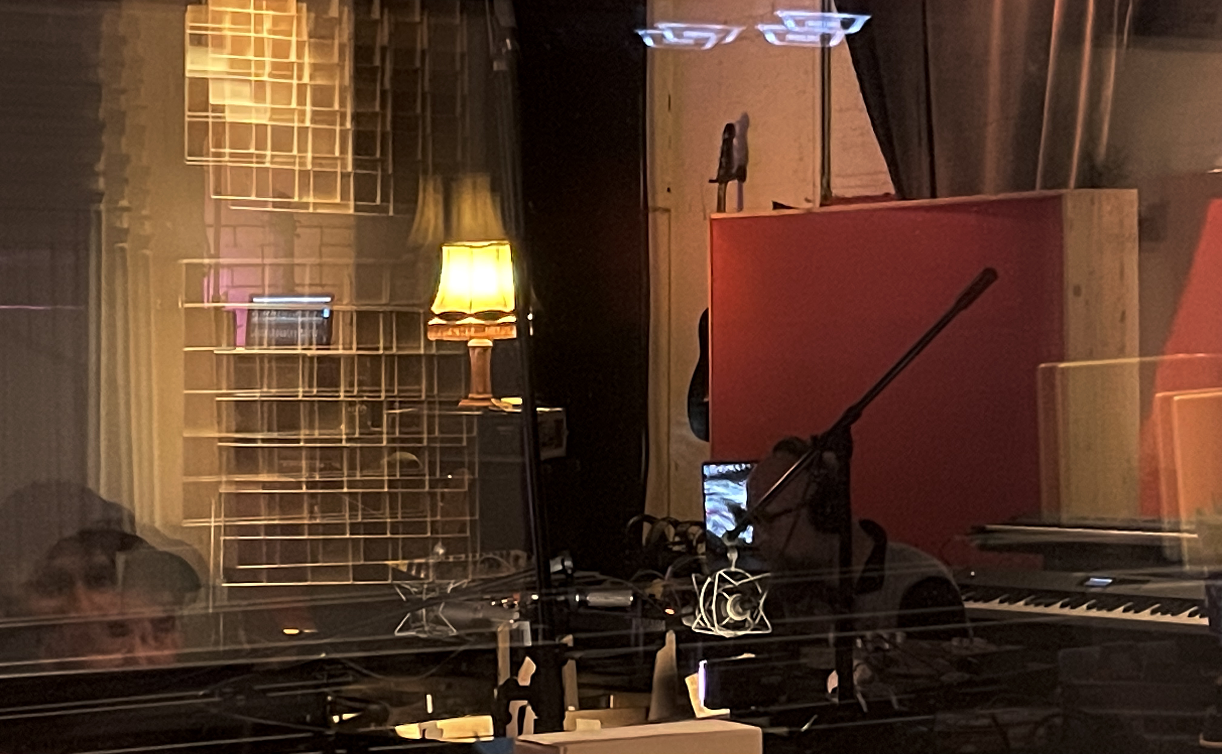 Einblick in ein Tonstudio: Musiker am Mikrofon, Klavier und Lampe im Hintergrund.