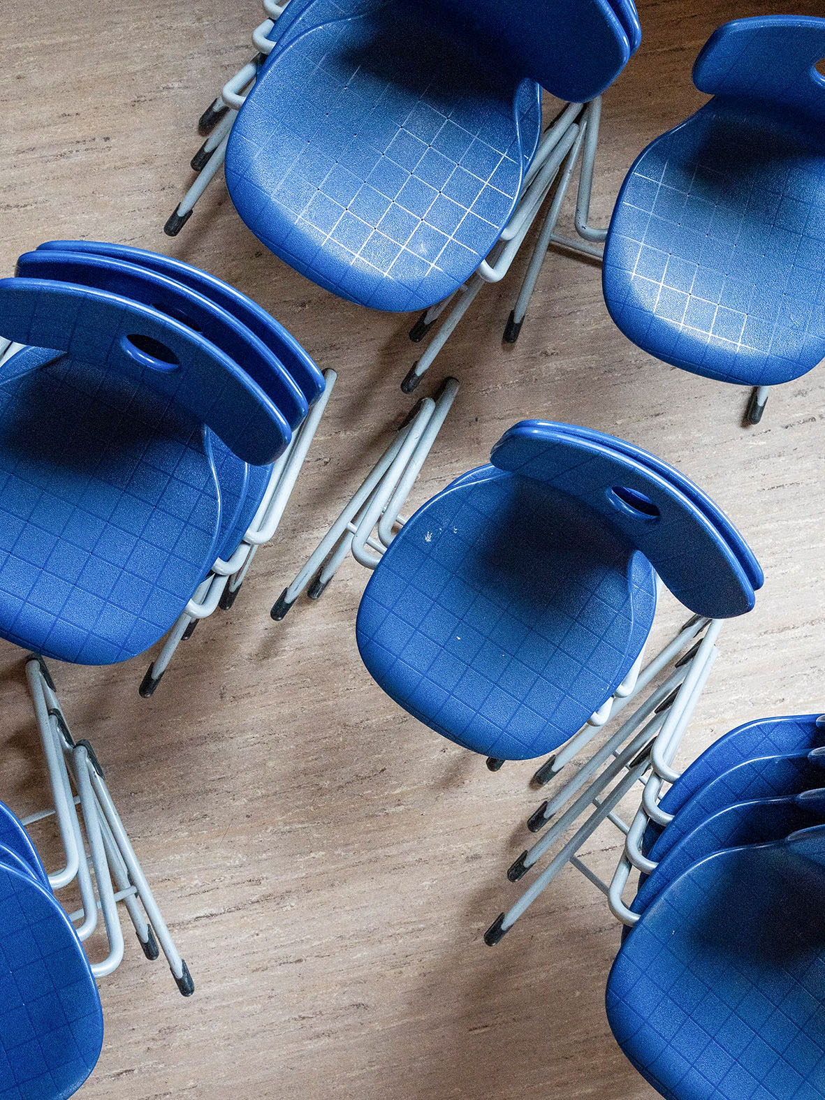 Stapel aus blauen Kunststoffstühlen mit Metallrahmen, aus Vogelperspektive auf einem Holzboden.
