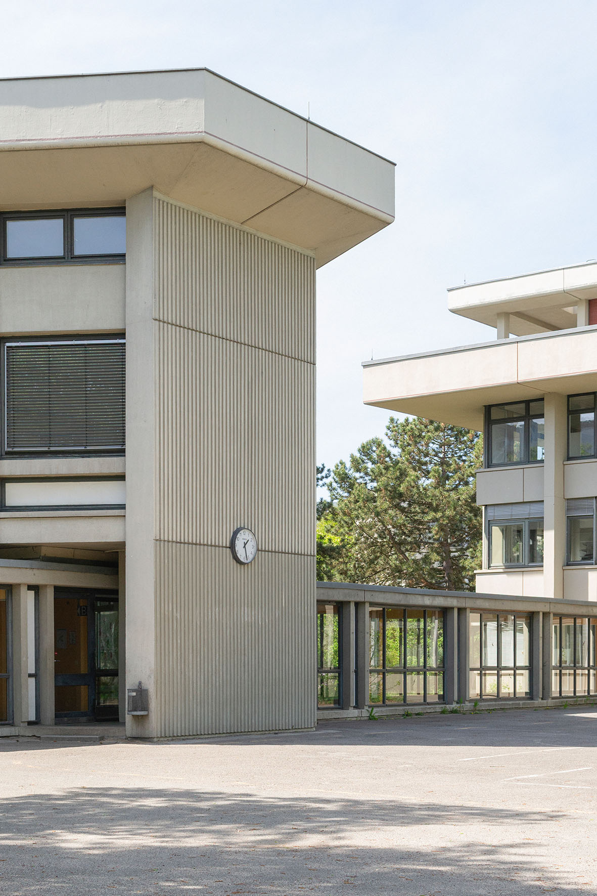 Modern architectural features of a building with a clock, window facades, and surroundings of trees and a parking lot.