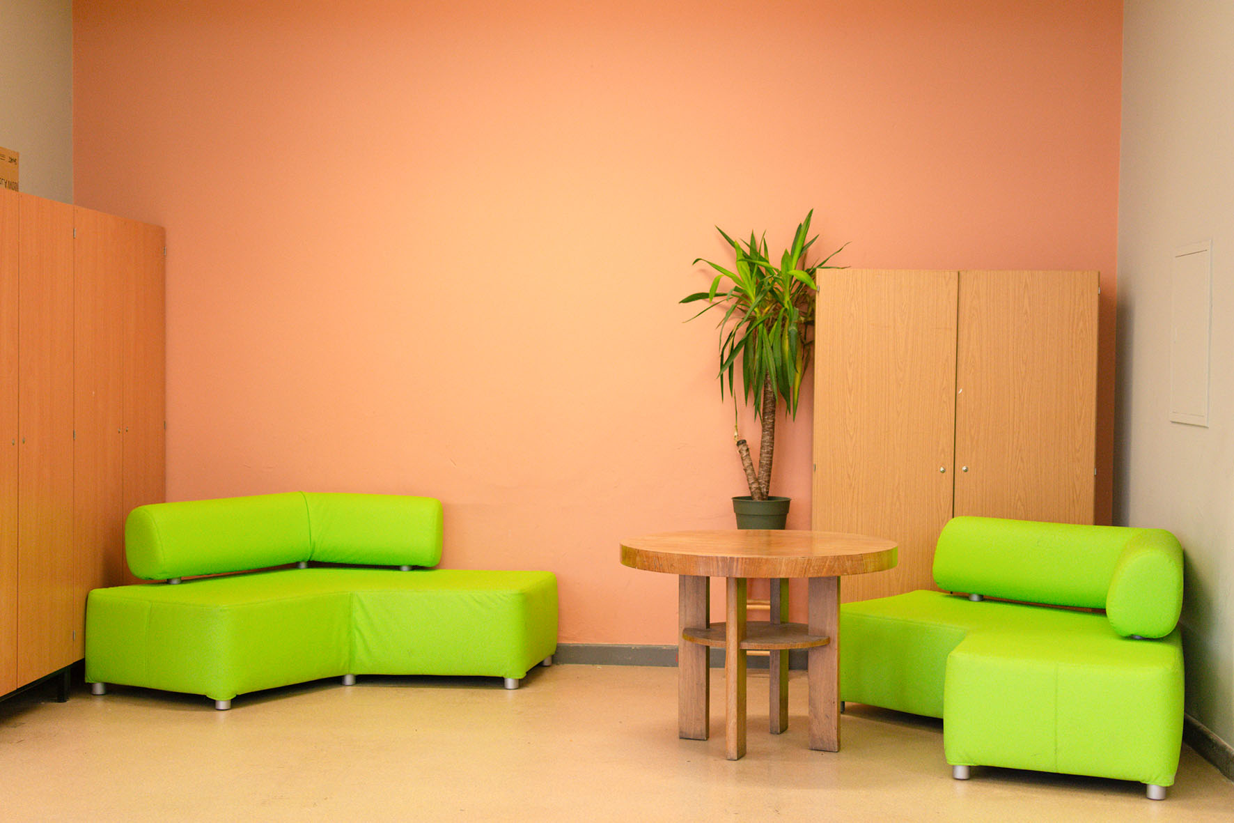 Futuristisch gestalteter Raum mit grünen Sofas, rundem Tisch und Pflanze vor rosa Wand.
