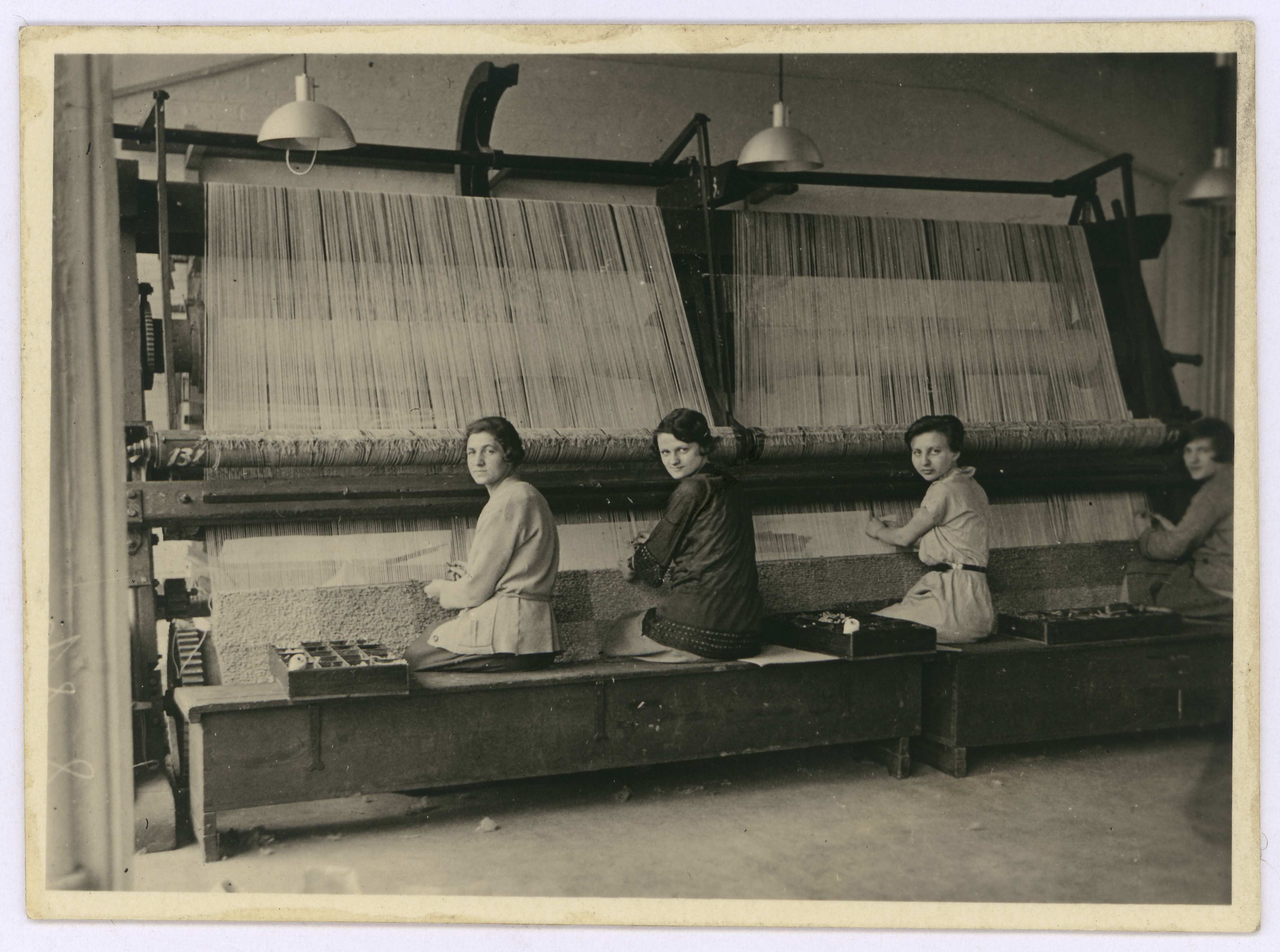 Frauen arbeiten an Webstühlen in einer Fabrik, umgeben von Maschinen und Materialien. Vintage Schwarzweißfoto.