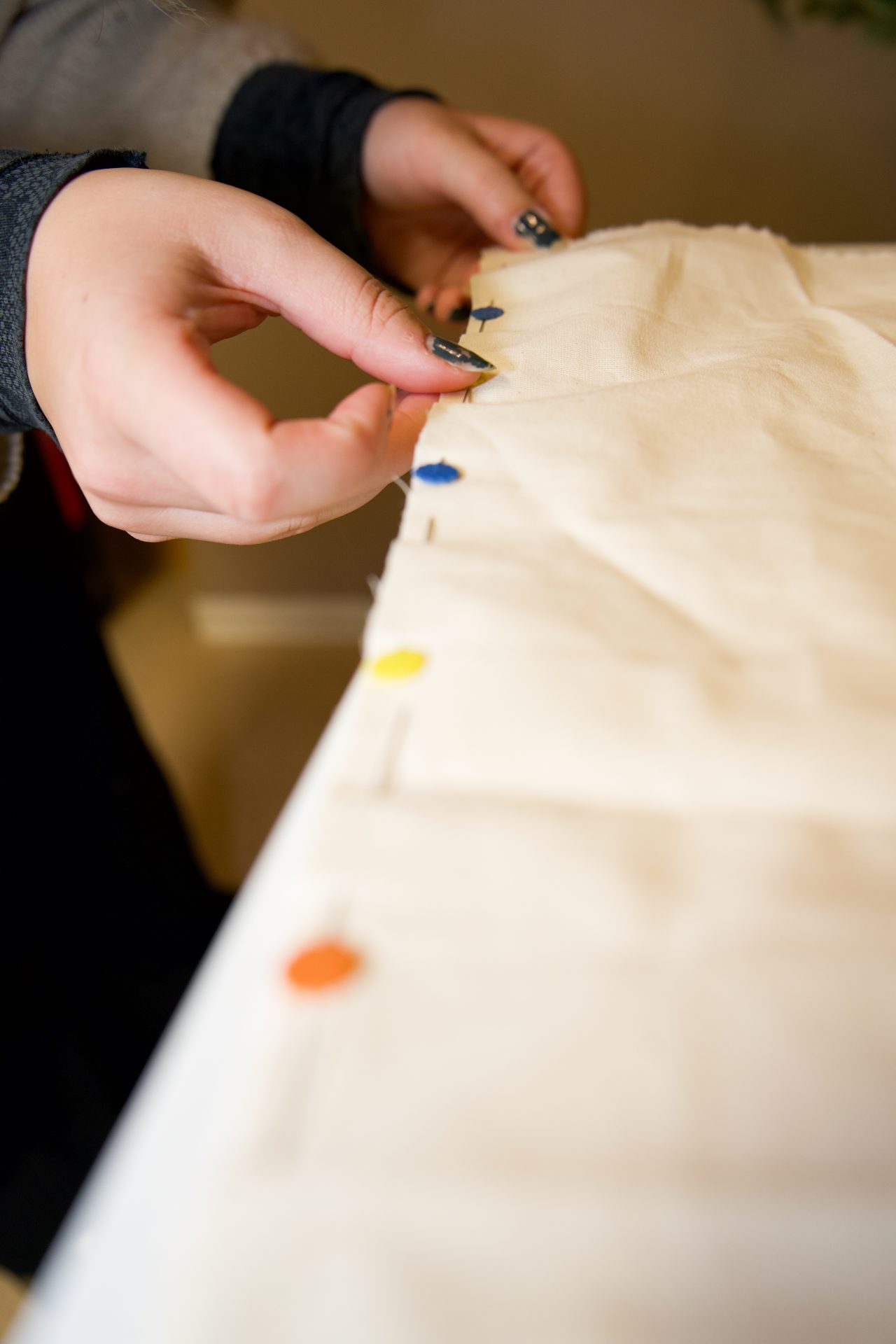 Hände stecken farbige Nadeln in einen weißen Stoffbereich für ein Nähprojekt.