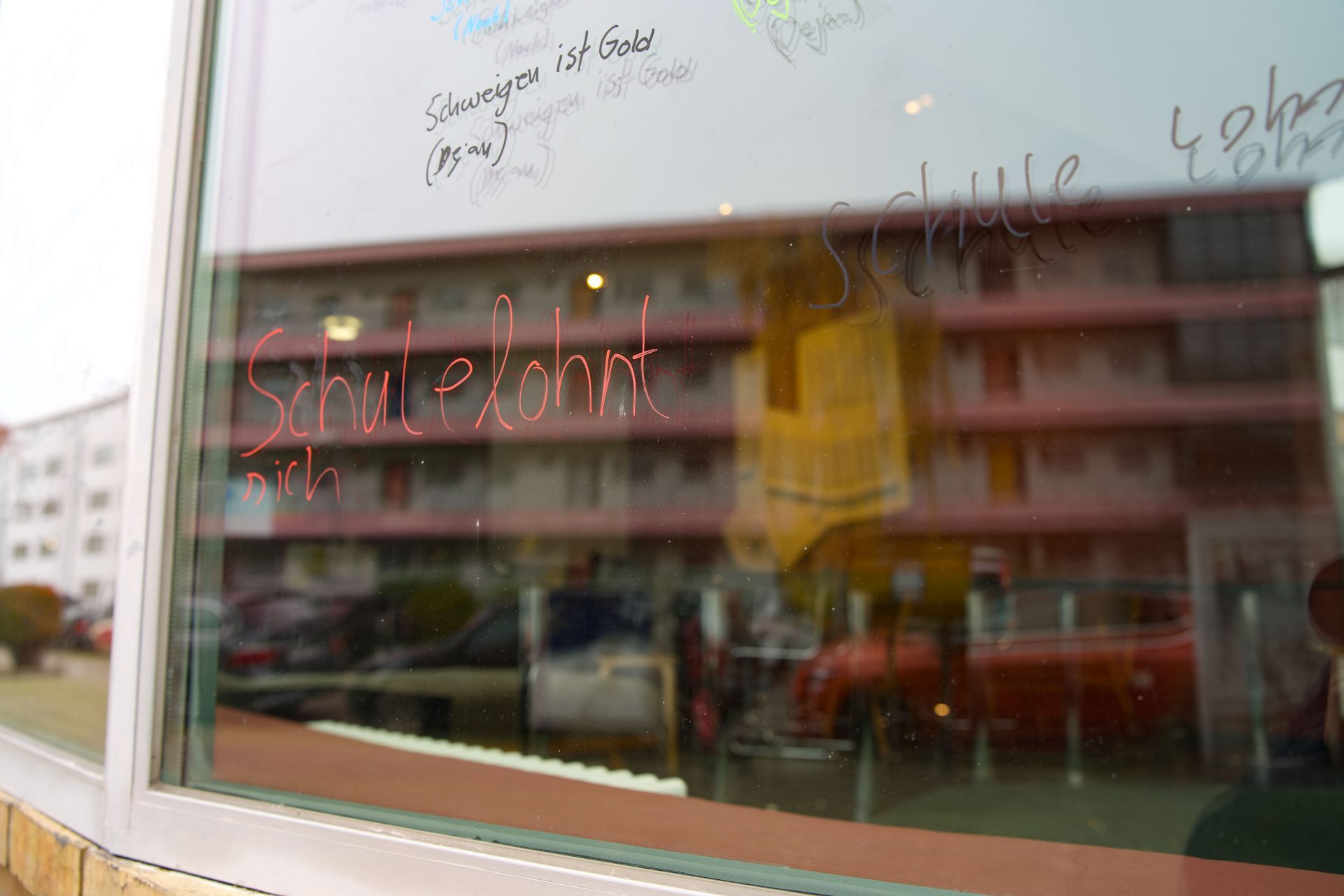 Graffiti on a window glass reading "School is worth it" and other colorful doodles.