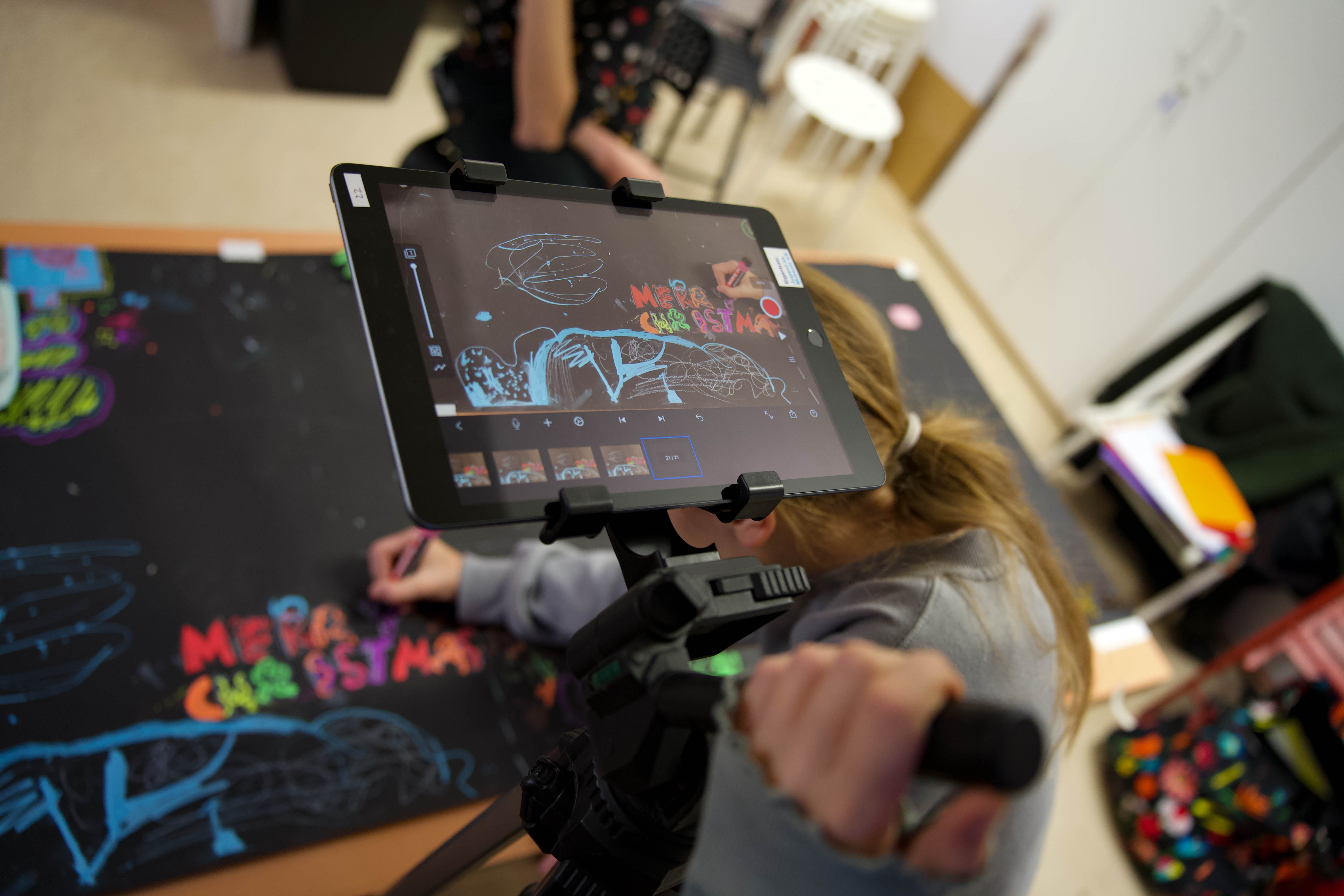 Tablet zeigt bunte Zeichnungen auf schwarzem Papier, während jemand mit einem Stift daran arbeitet. Kreative Tätigkeit.