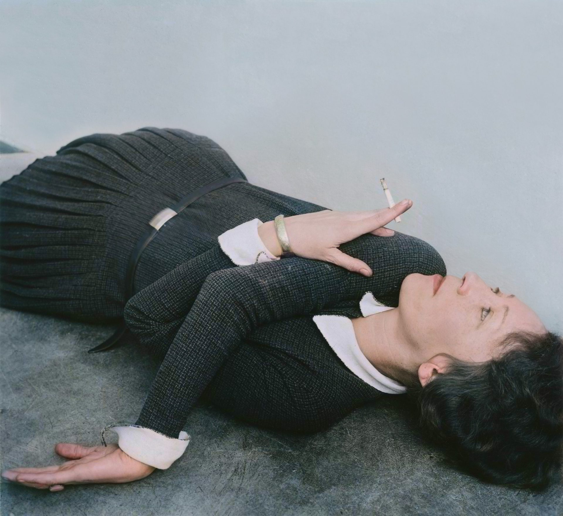 Eine Frau mit Zigarette liegt in markantem Winkel auf dem Boden, abgebildet in einem kontrastreichen Schwarz-Weiß-Foto.