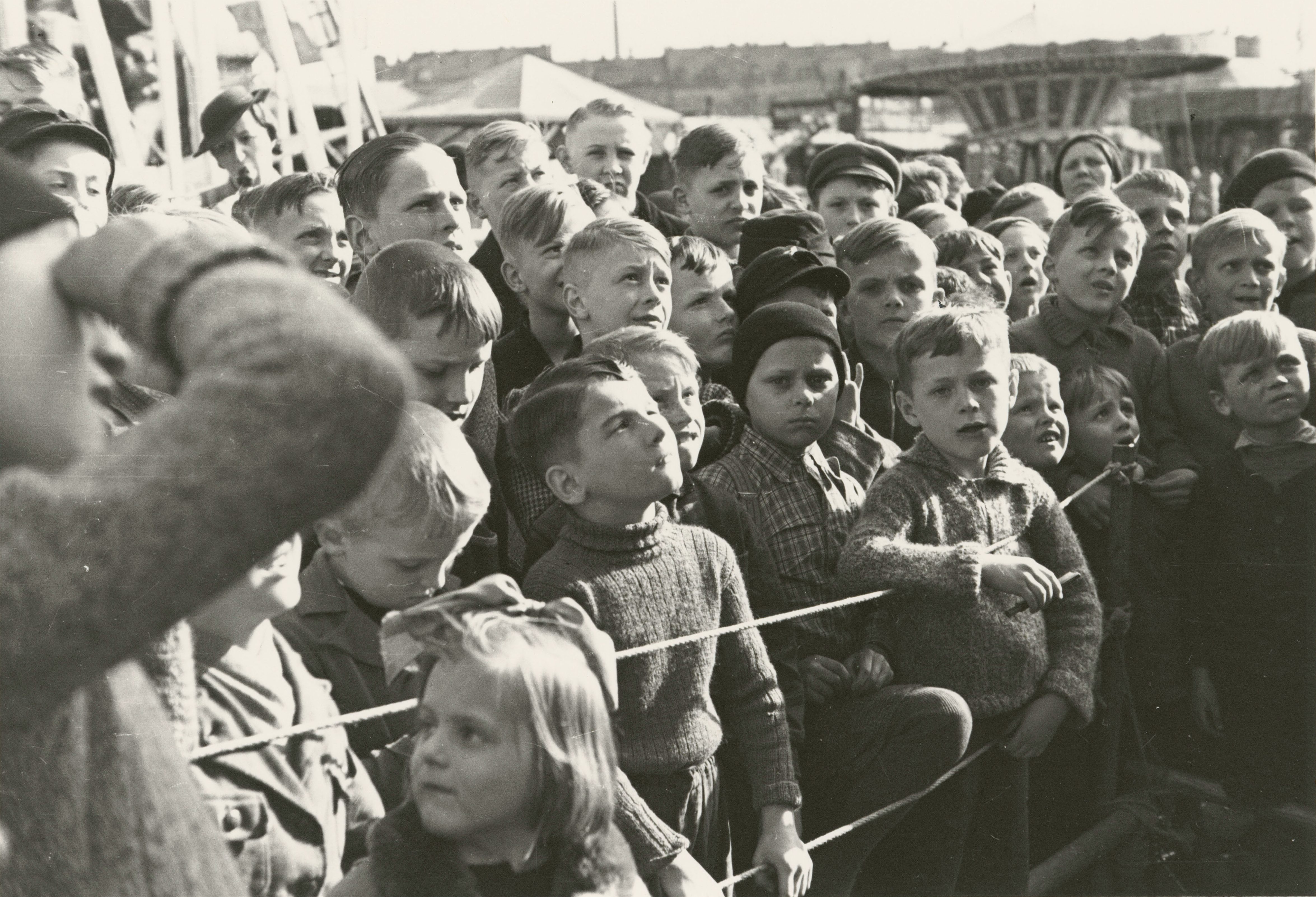 Eine Gruppe neugieriger Kinder beobachtet aufmerksam eine Veranstaltung im Freien.