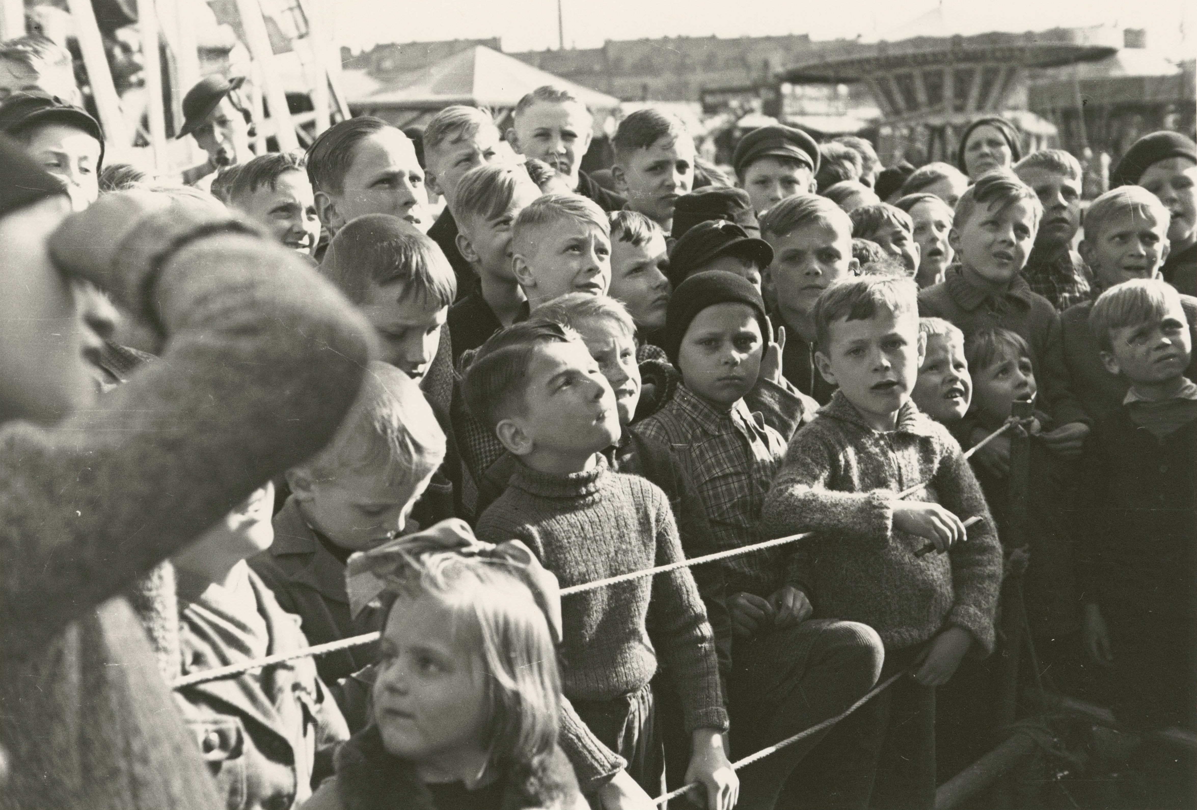 A group of curious and attentive children watches an outdoor event.