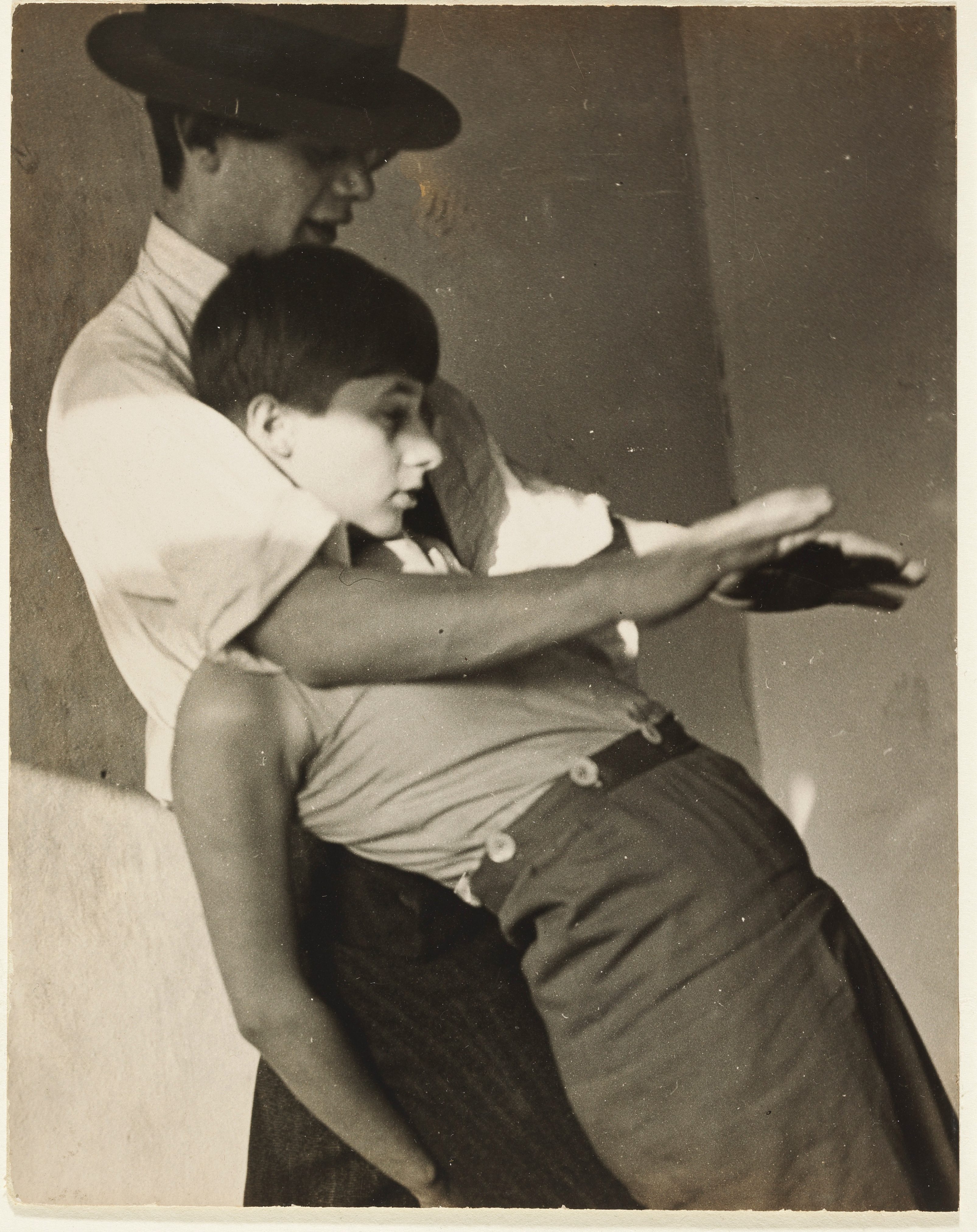 Ein Mann umarmt eine Frau in eleganter Pose, festgehalten in einer sepiafarbenen Fotografie.