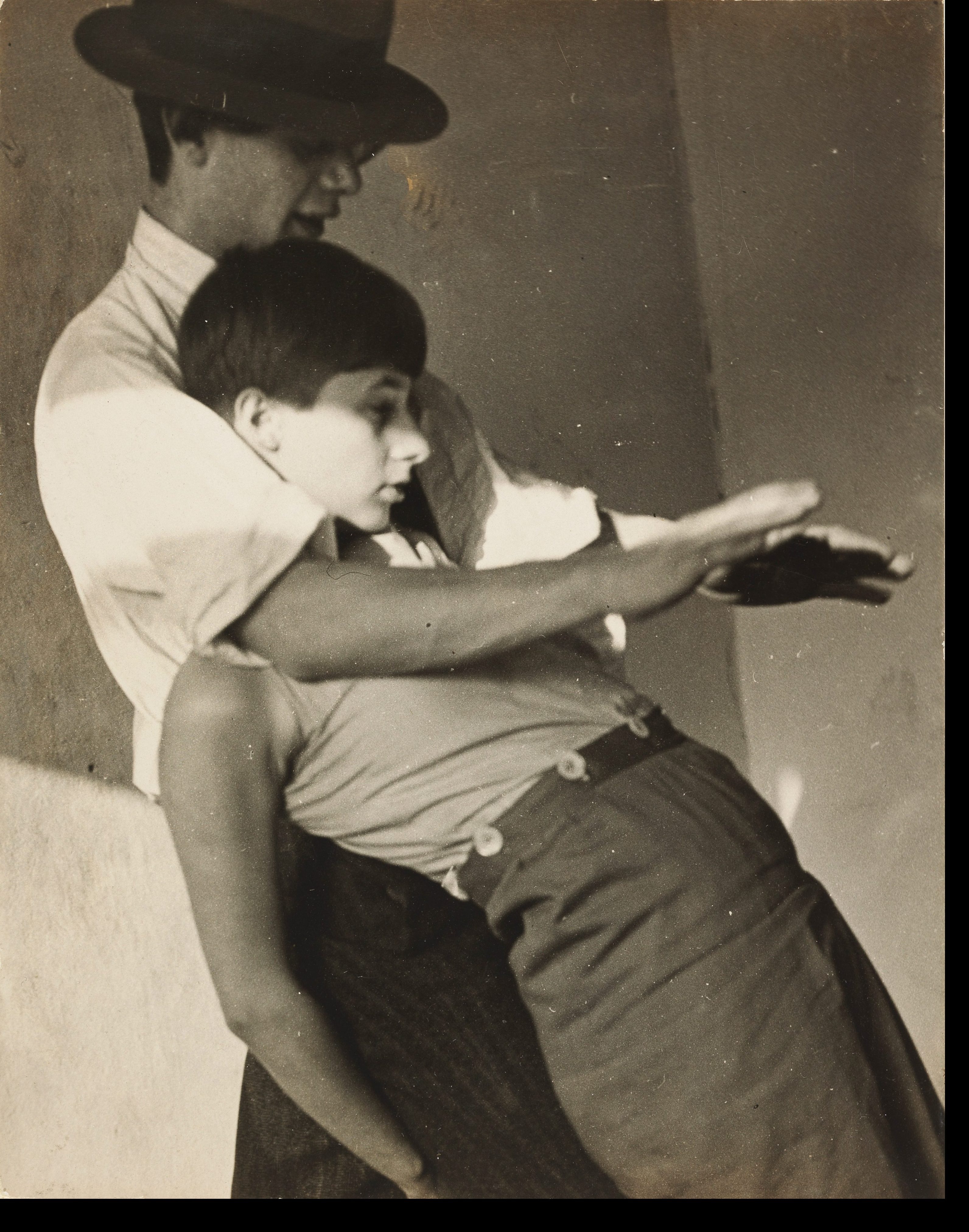 A man embraces a woman as she strikes an elegant pose in a sepia-toned photograph.