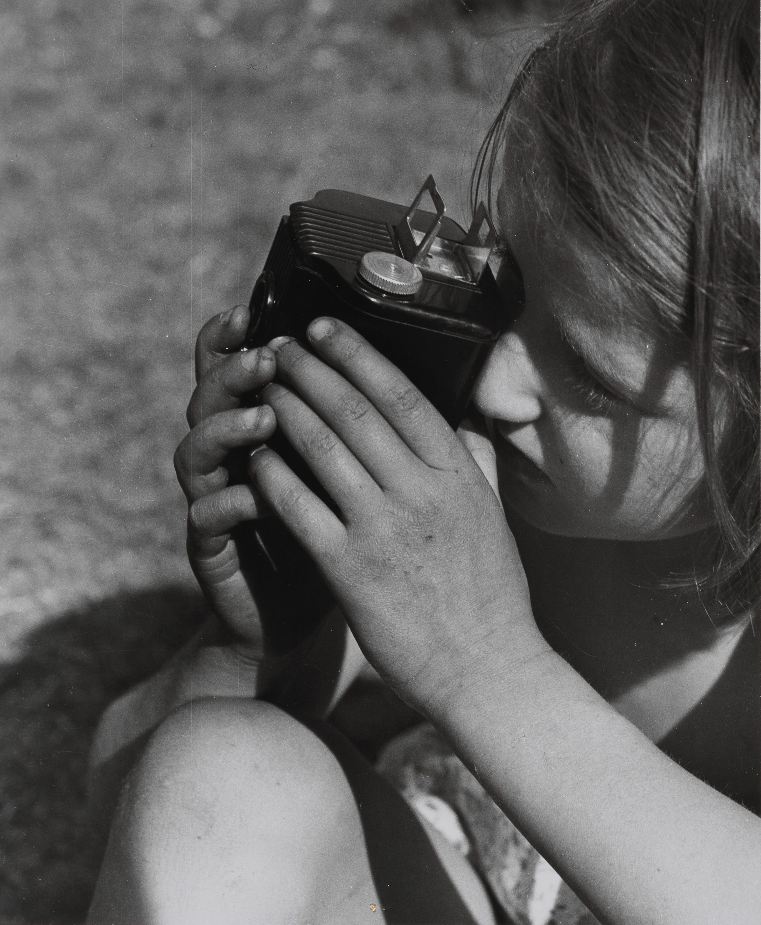A girl holds a camera close to her face and watches through the viewfinder, with a blurred background.