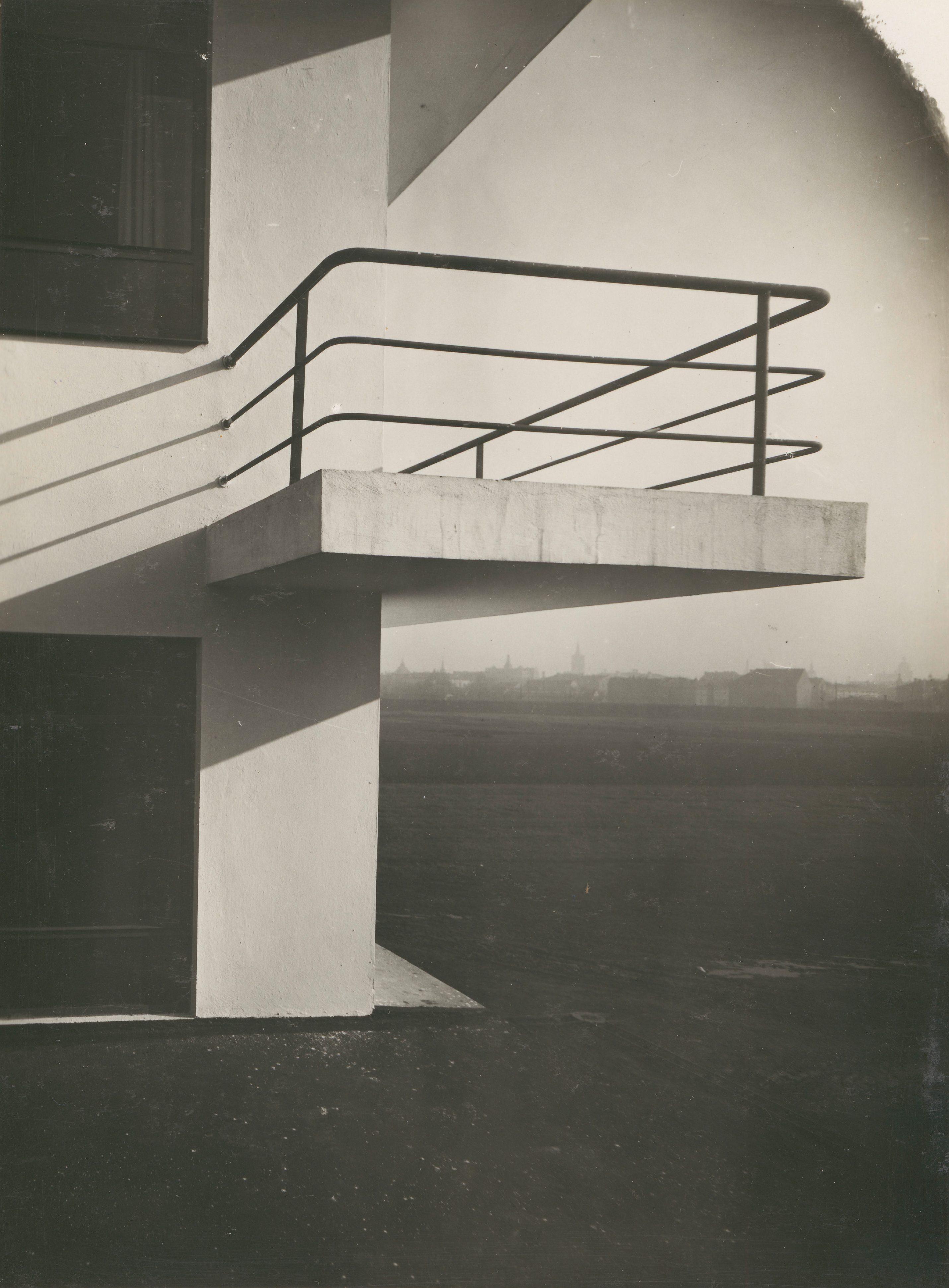 Black metal railings around a concrete balcony of a modern building, with a blurry cityscape in the background.