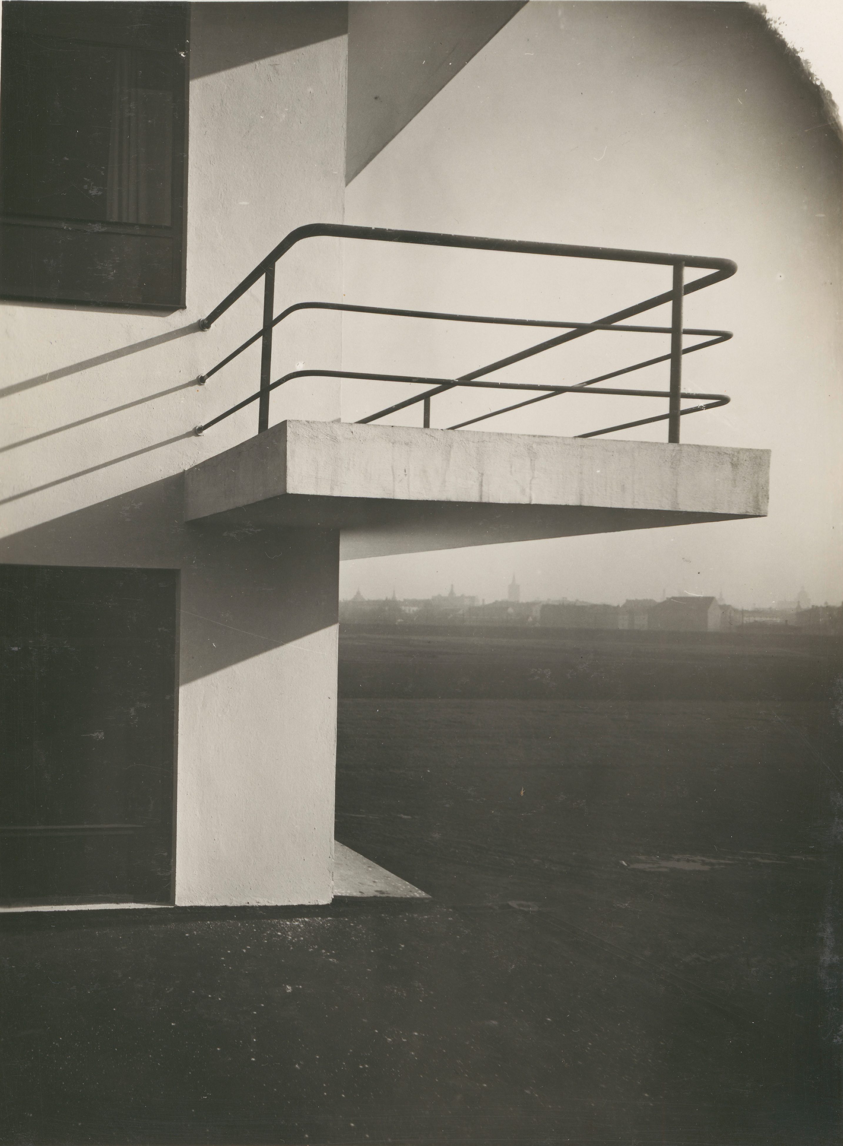 Schwarze Metallgeländer um einen betonierten Balkon eines modernen Gebäudes, im Hintergrund eine verschwommene Stadtlandschaft.