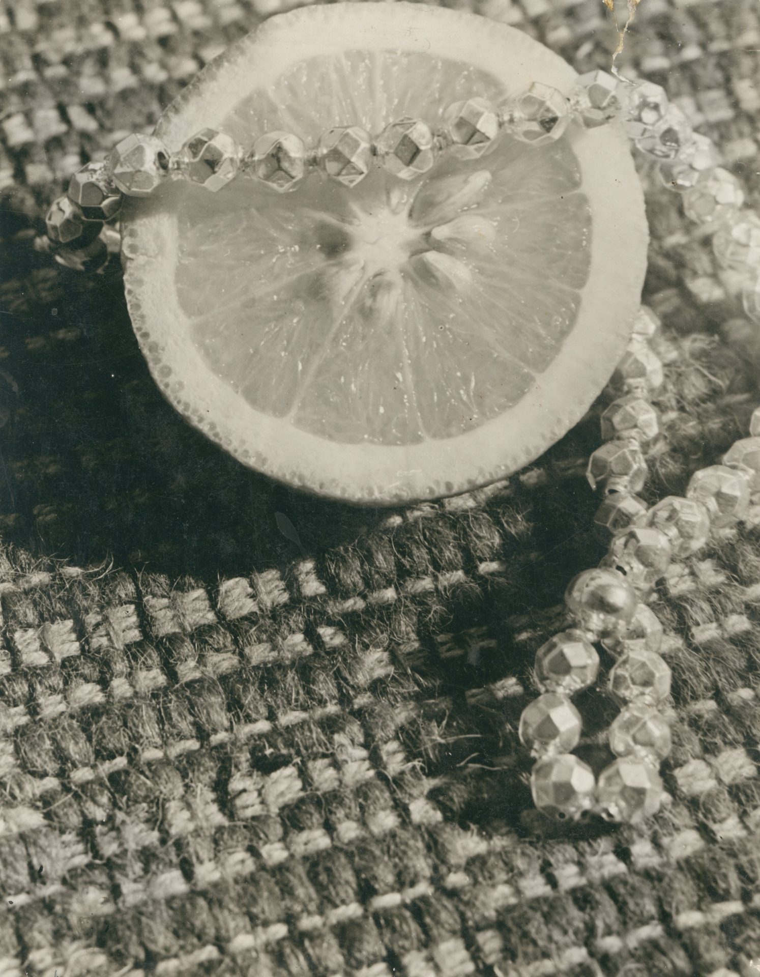 Scheibe einer Zitrone auf geflochtenem Untergrund, umgeben von facettierten Perlen.