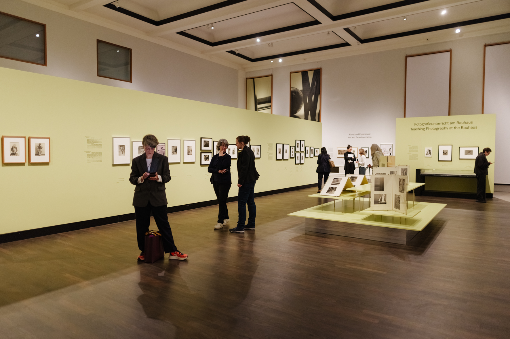 Besucher erkunden eine Galerie mit Fotografien, umgeben von hellgrünen Wänden und zeitgenössischen Ausstellungsstücken.
