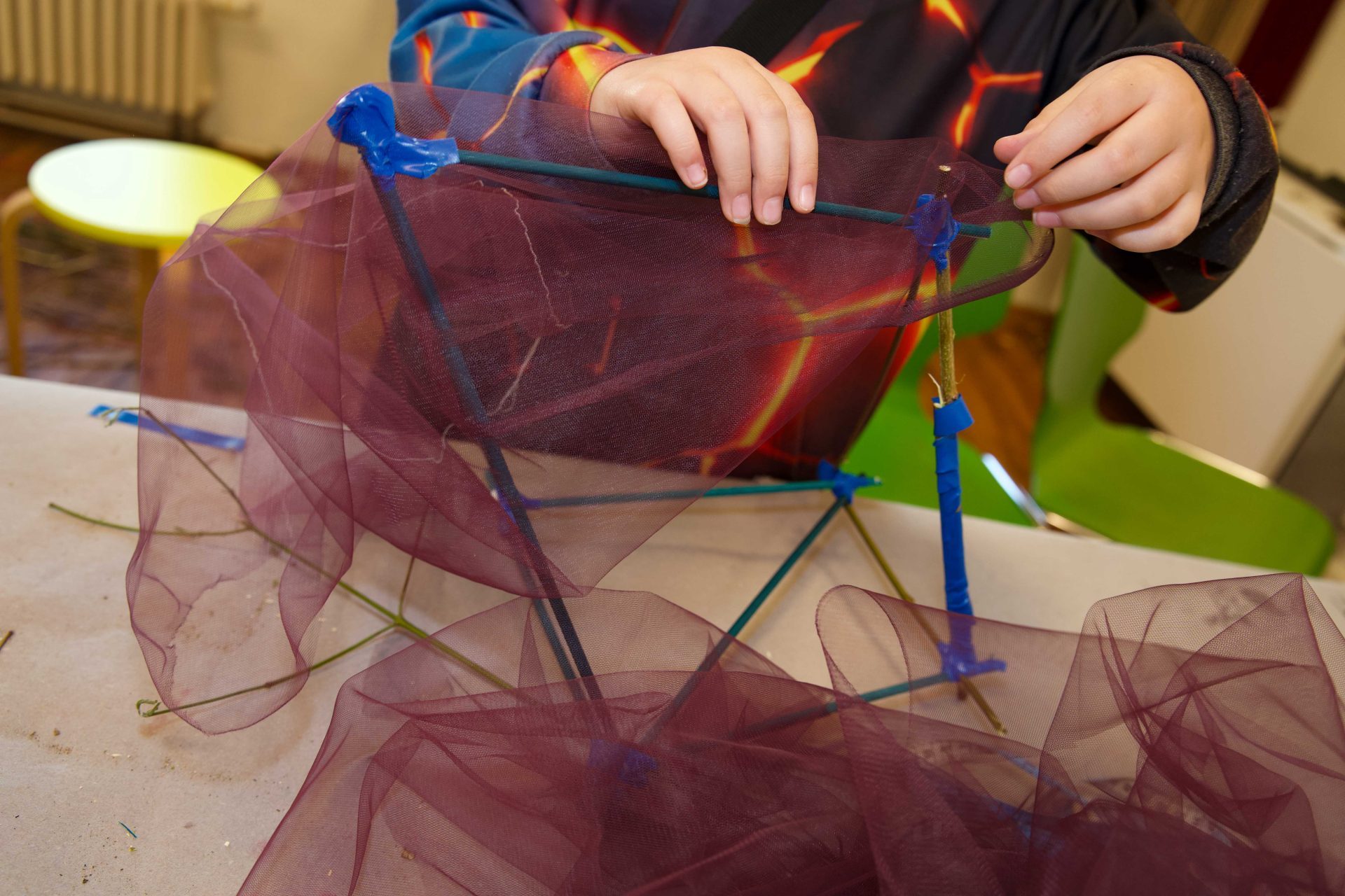 A child builds a three-dimensional structure with colorful wires and purple tulle.