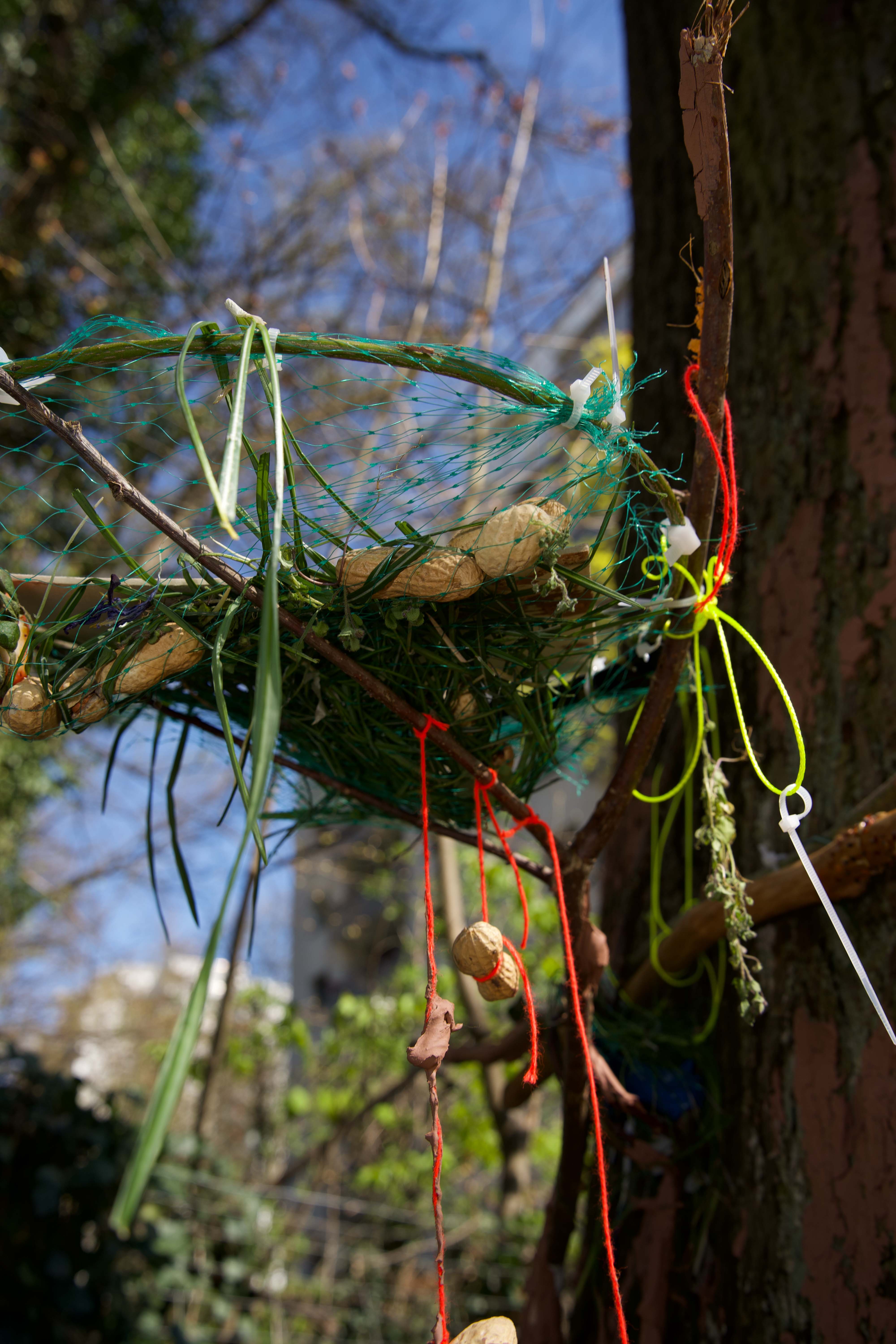 Buntes, hängendes Kunstwerk aus Naturmaterialien, Ästen und bunten Schnüren im Freien.