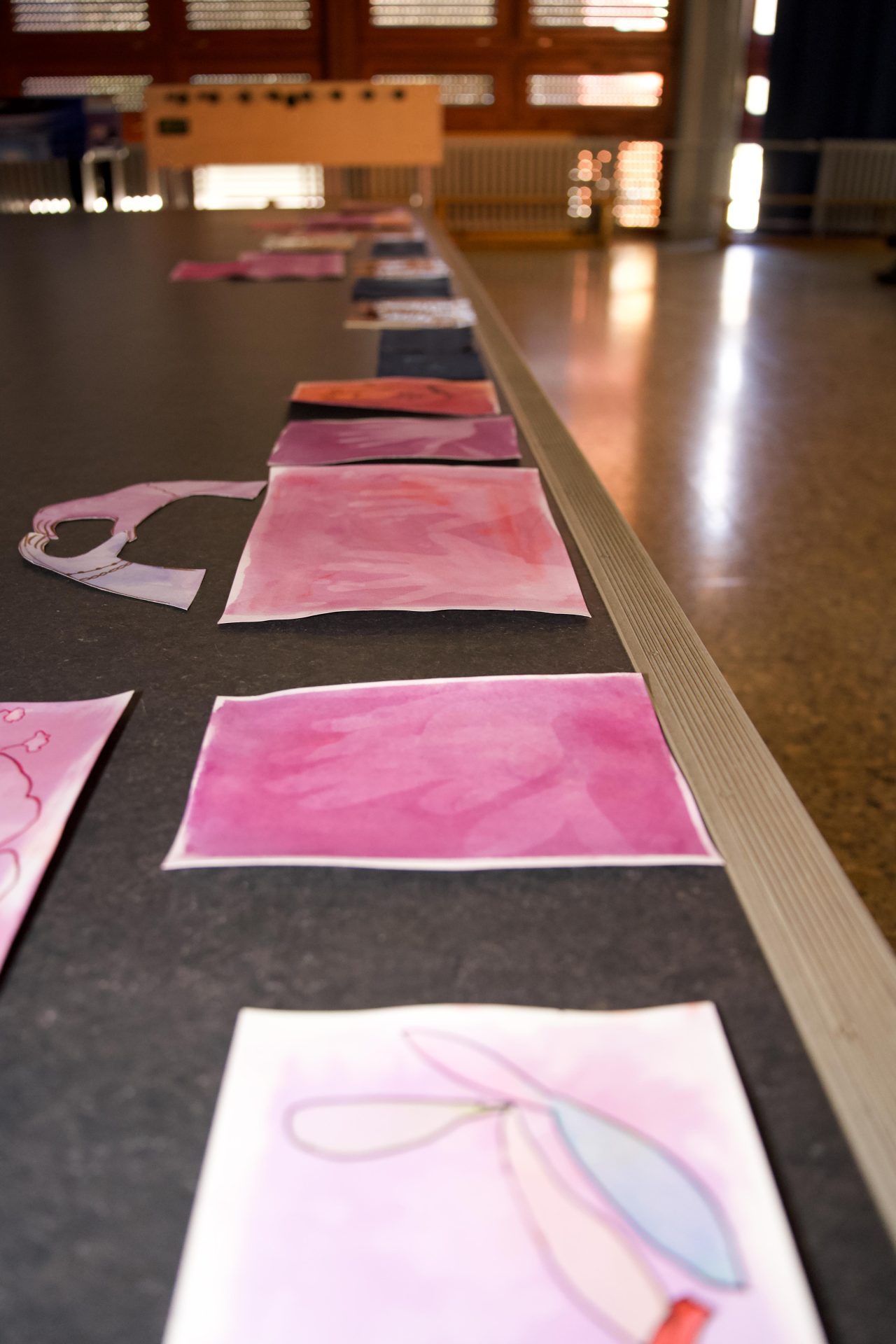 A series of watercolor paintings in various shades of pink and purple on a table.