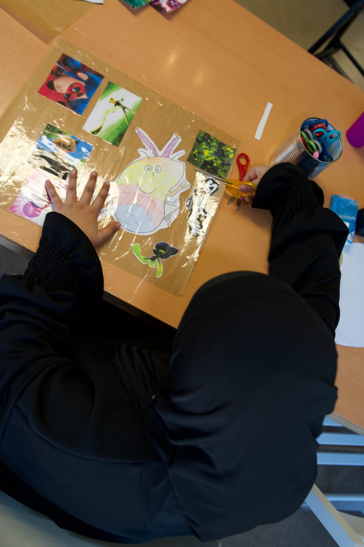 A child is working on a craft project with pictures and scissors on a table.