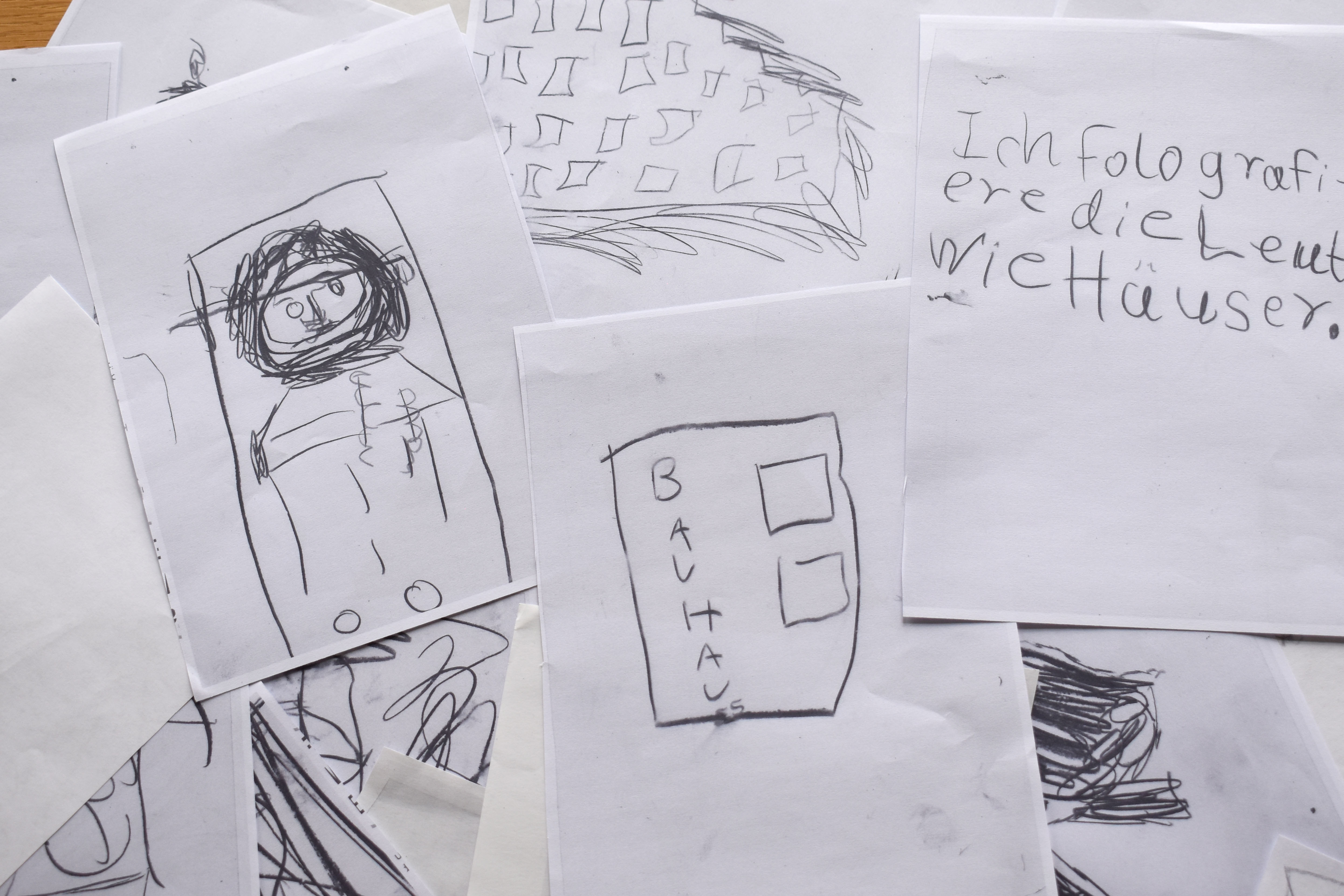 Kinderzeichnungen auf Papier mit einem Menschen und dem Wort "Bauhaus" darunter.