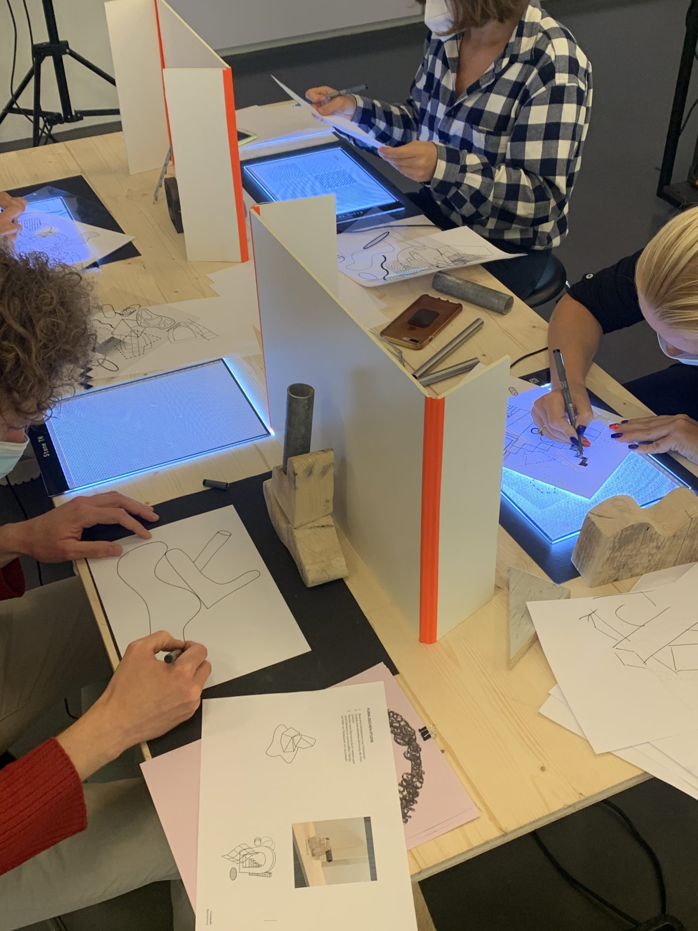 Zu sehen ist eine Workshop-Situation. Man erkennt Hände über eine Tischplatte, die sowohl mit digitalen als auch mit analogen Mitteln arbeiten.
