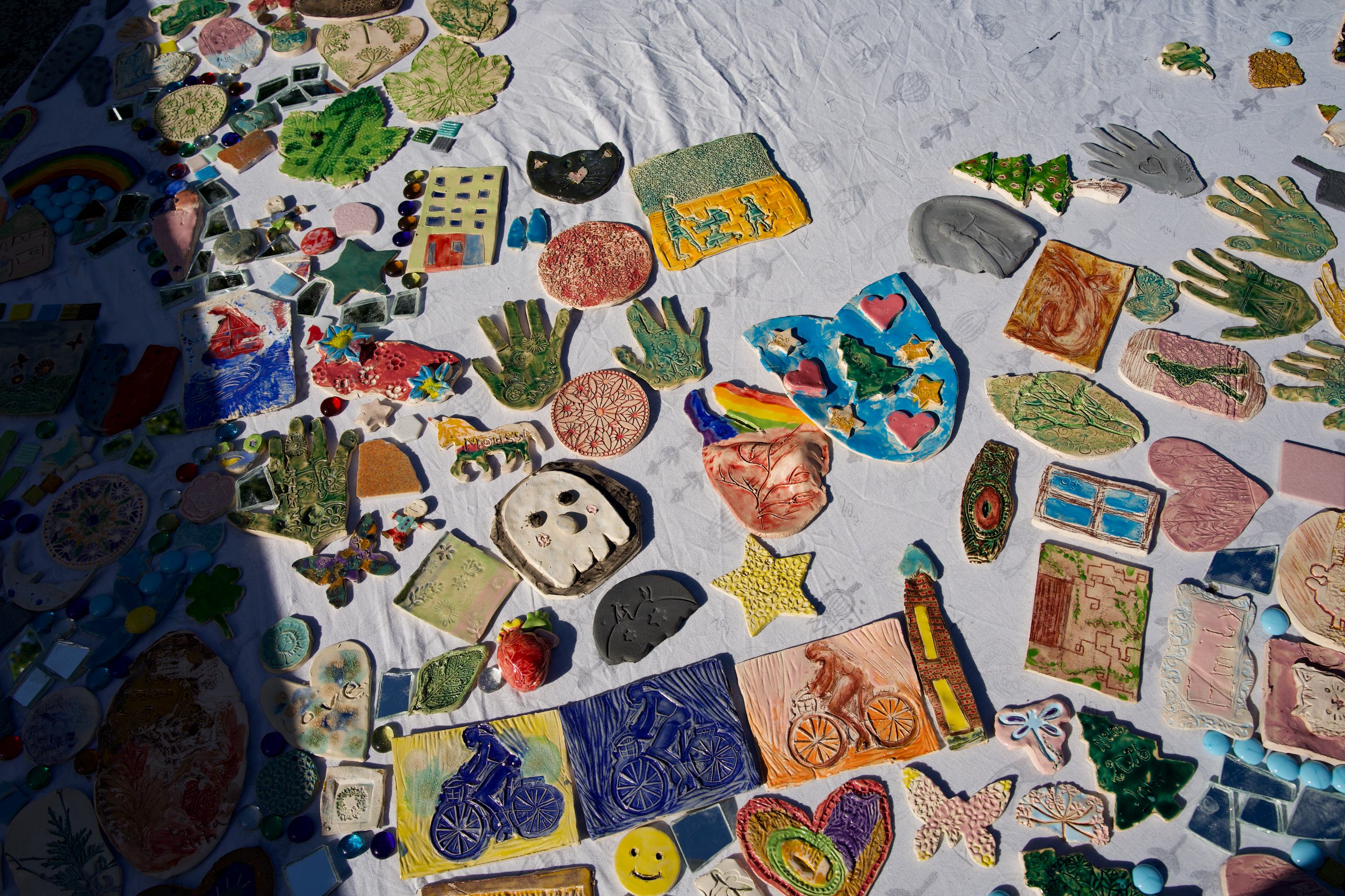 Bunte, handgefertigte Keramiken und Mosaike auf einem weißen Tisch, mit vielfältigen Formen und Designs.