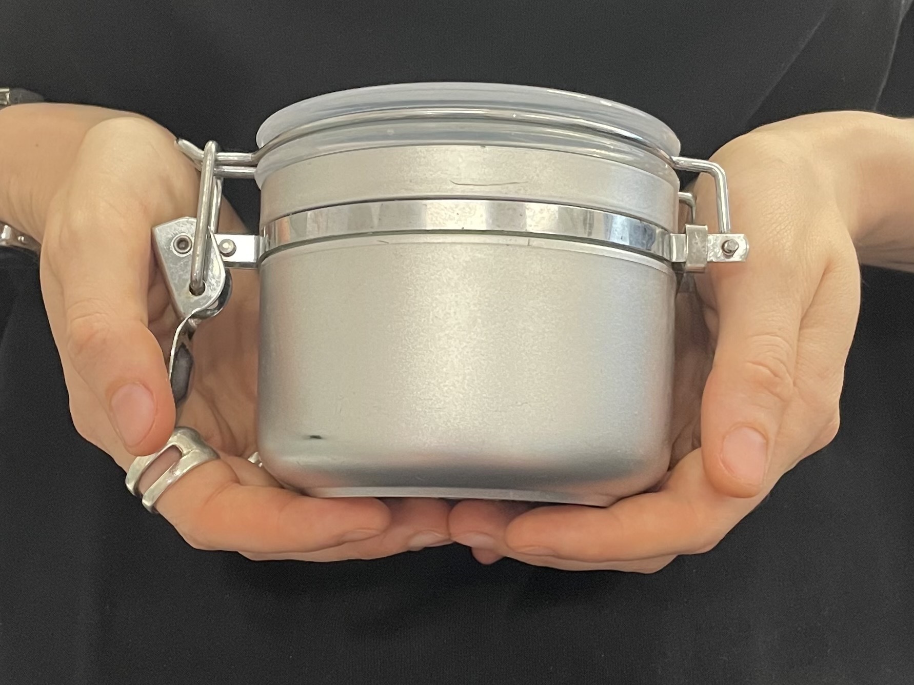 Zwei Hände halten ein silbern lackiertes Glas mit Bügelverschluss.